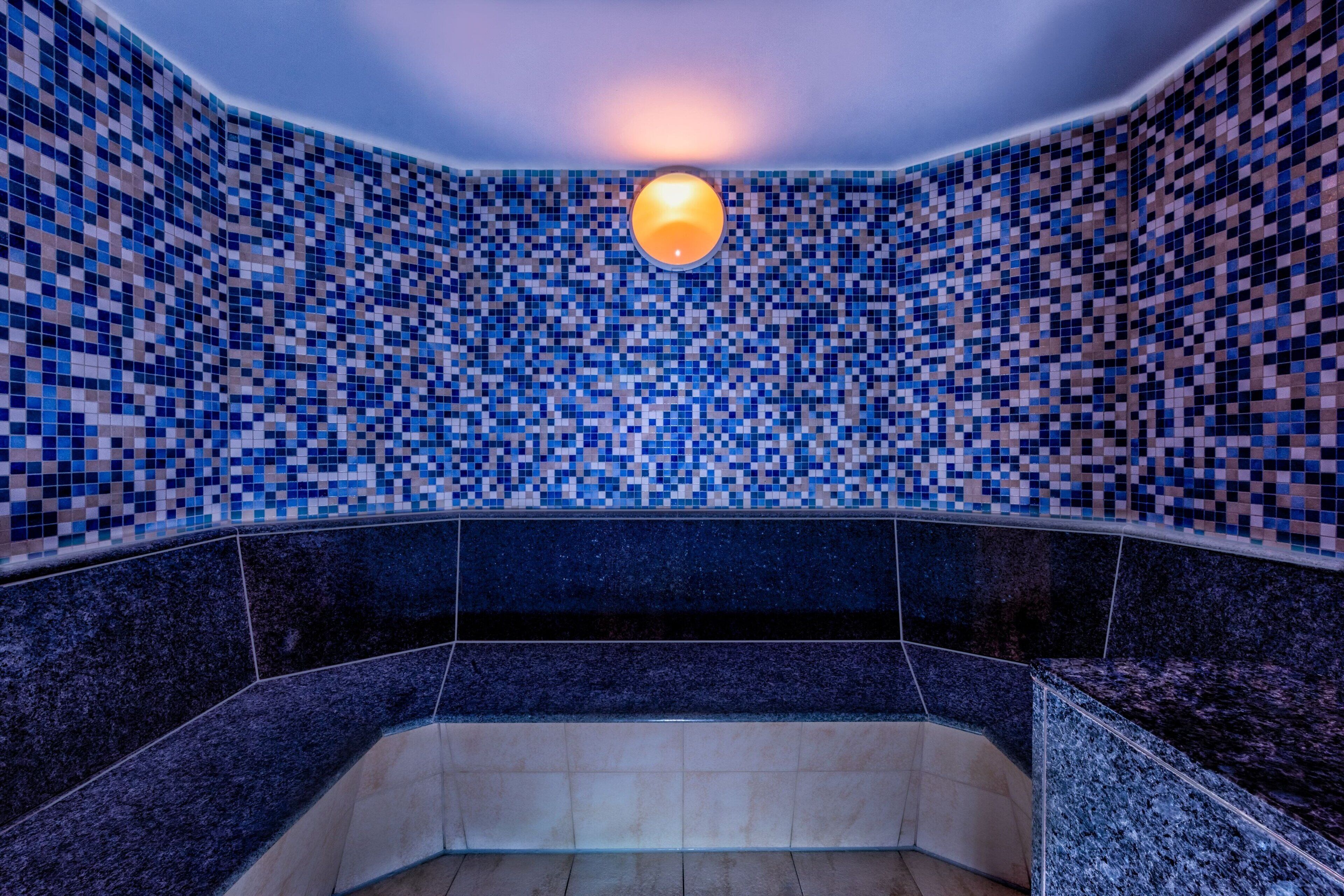 Un baño con paredes de mosaico y una lámpara central.