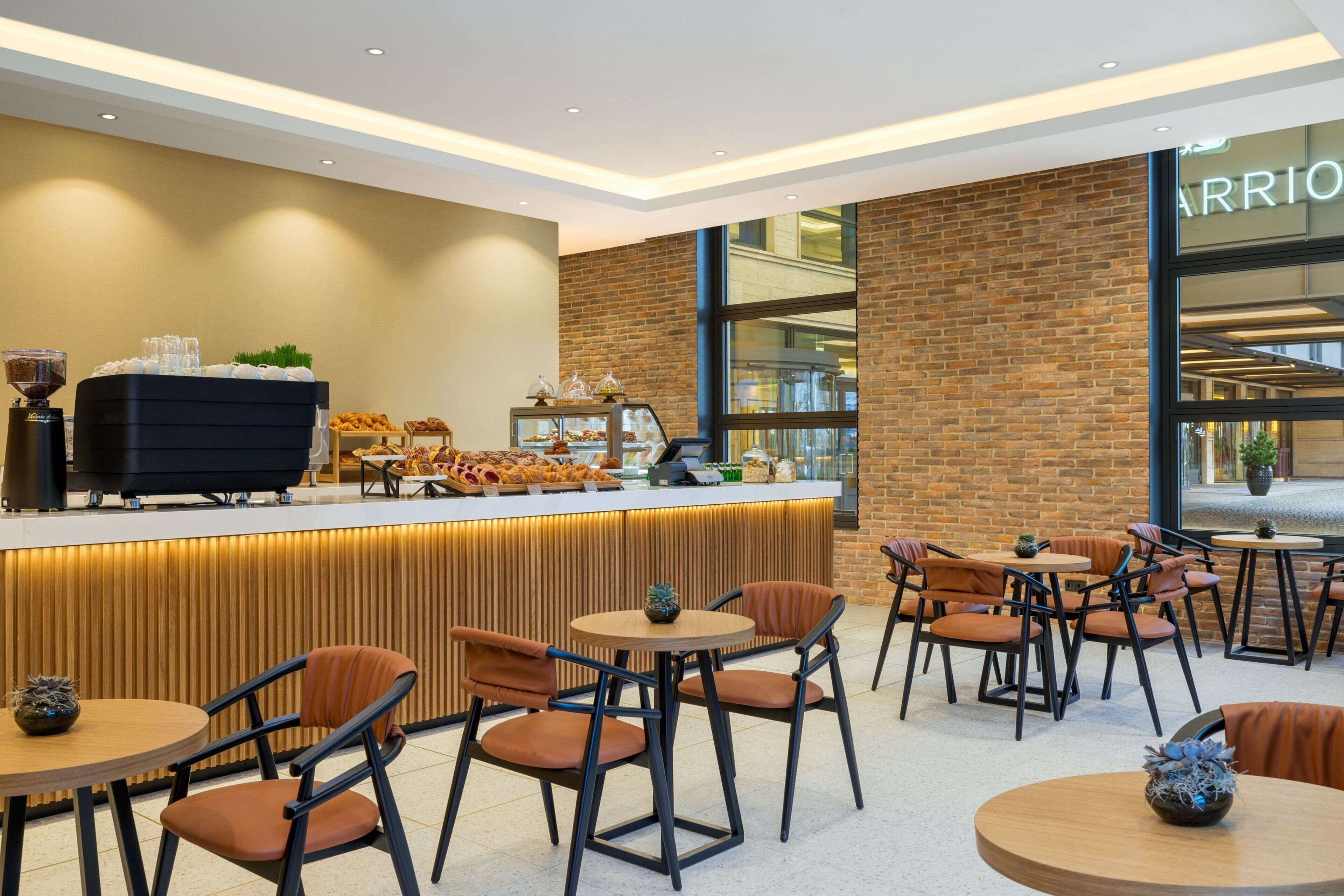 A modern cafe with a coffee station, seating area, and a view of the Marriott hotel.