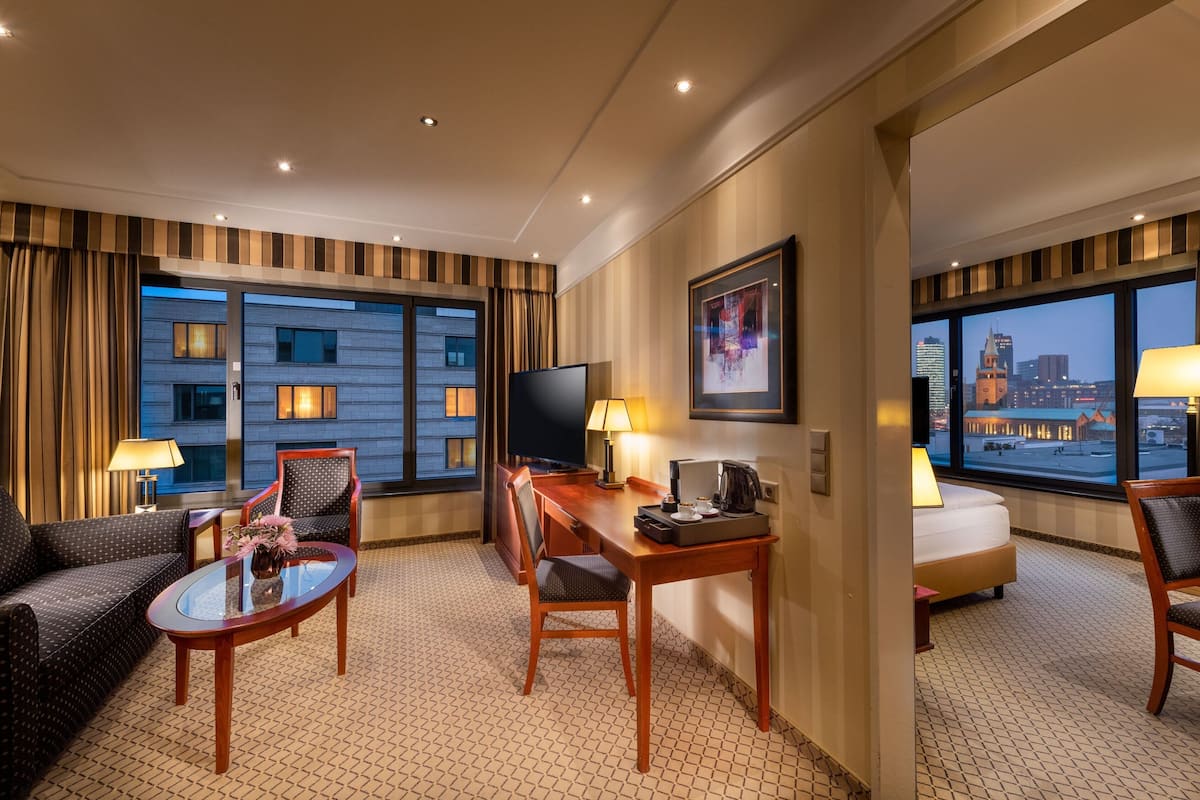 Ein Hotelzimmer mit großem Fenster, einem Flachbildfernseher, einem Schreibtisch mit Lampe, einer Couch und einem Bett.
