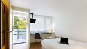 Habitación de hotel con cama, escritorio con computadora portátil, silla, ventana con cortinas y puerta que da al exterior.