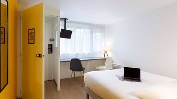 A hotel room with a bed, a desk with a laptop, a chair, a window with curtains, and a door.