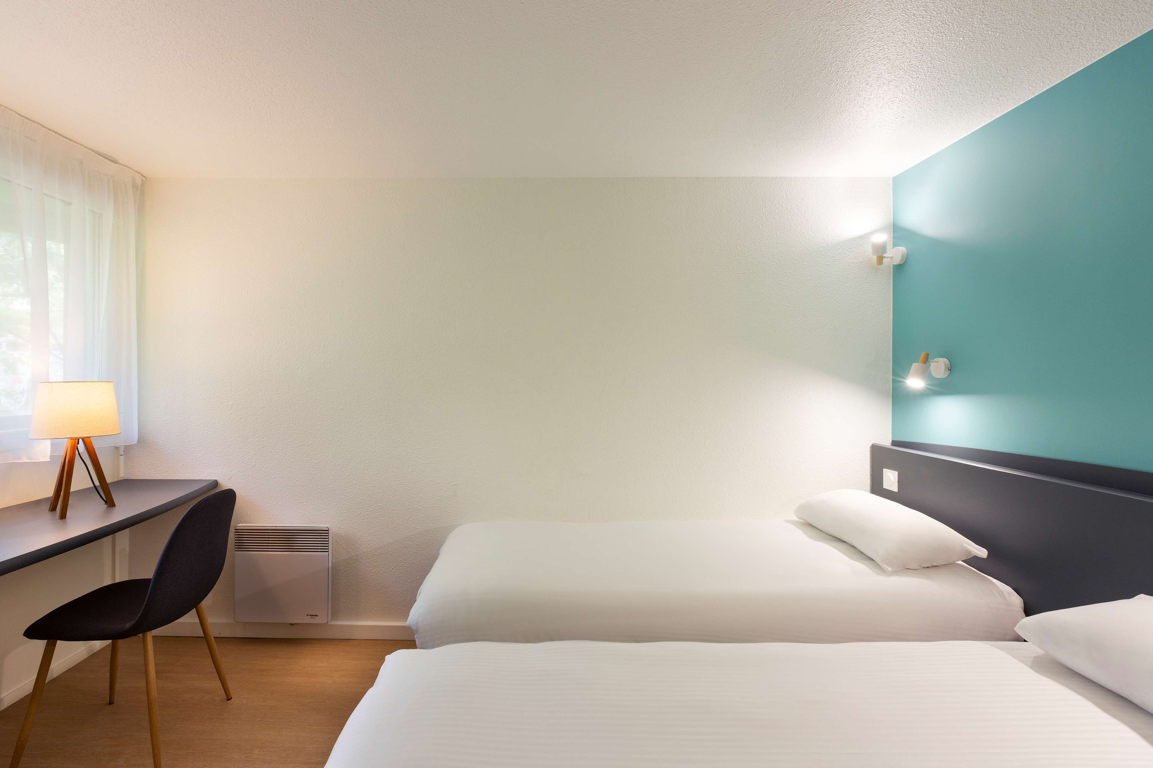 Una habitación de hotel con cama, escritorio, silla y lámpara de pared.