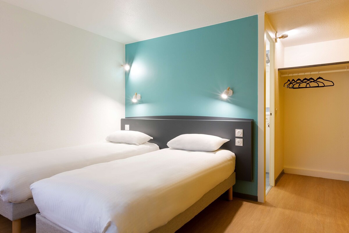 Una habitación con dos camas individuales, una pared de acento color turquesa y un perchero.