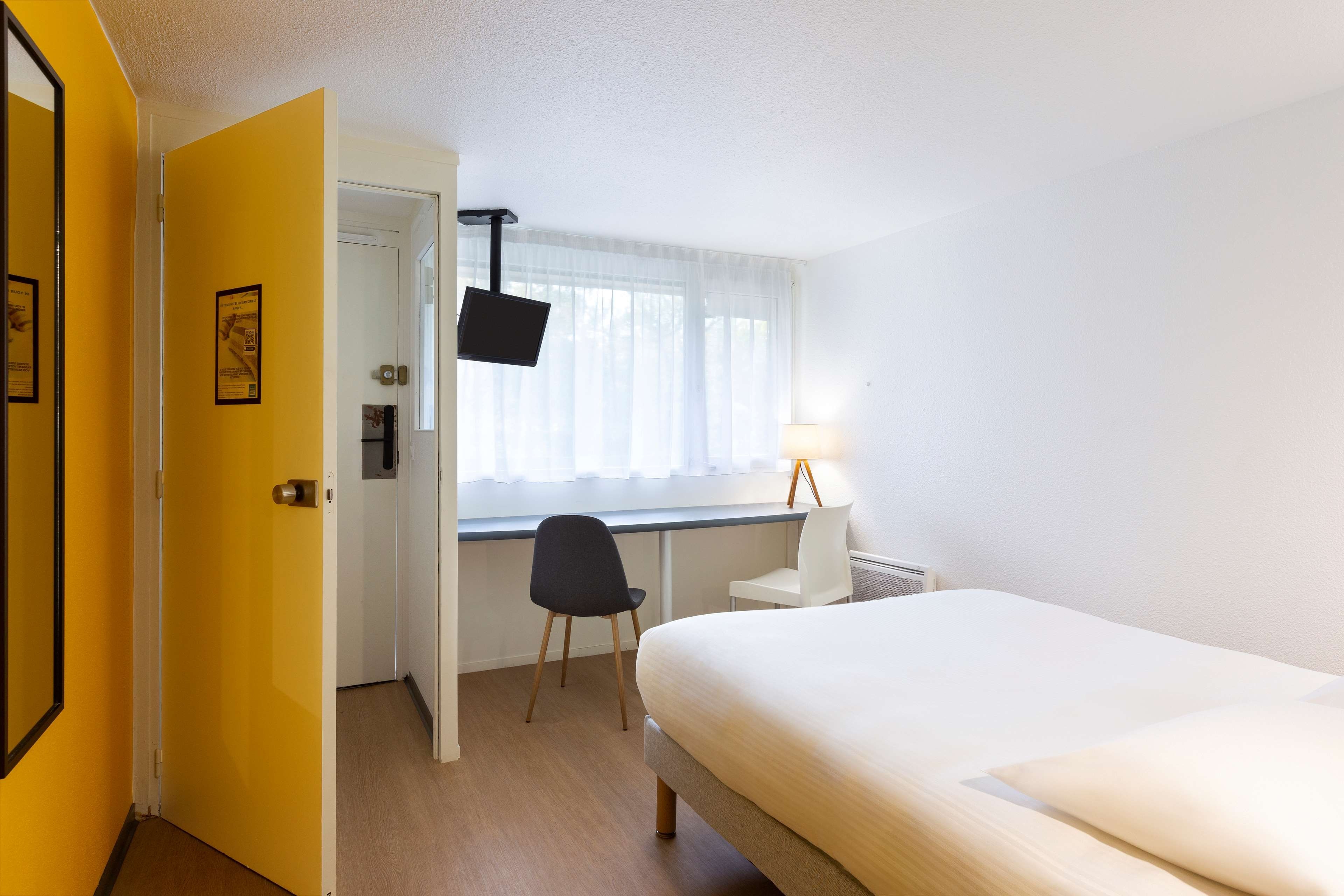 A hotel room with a bed, a desk, a chair, a window with curtains, and a door.