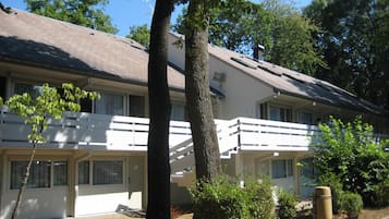 Un motel à deux étages, à l’extérieur blanc, doté d’un porche avant couvert et d’un petit jardin avec un arbre et des arbustes.