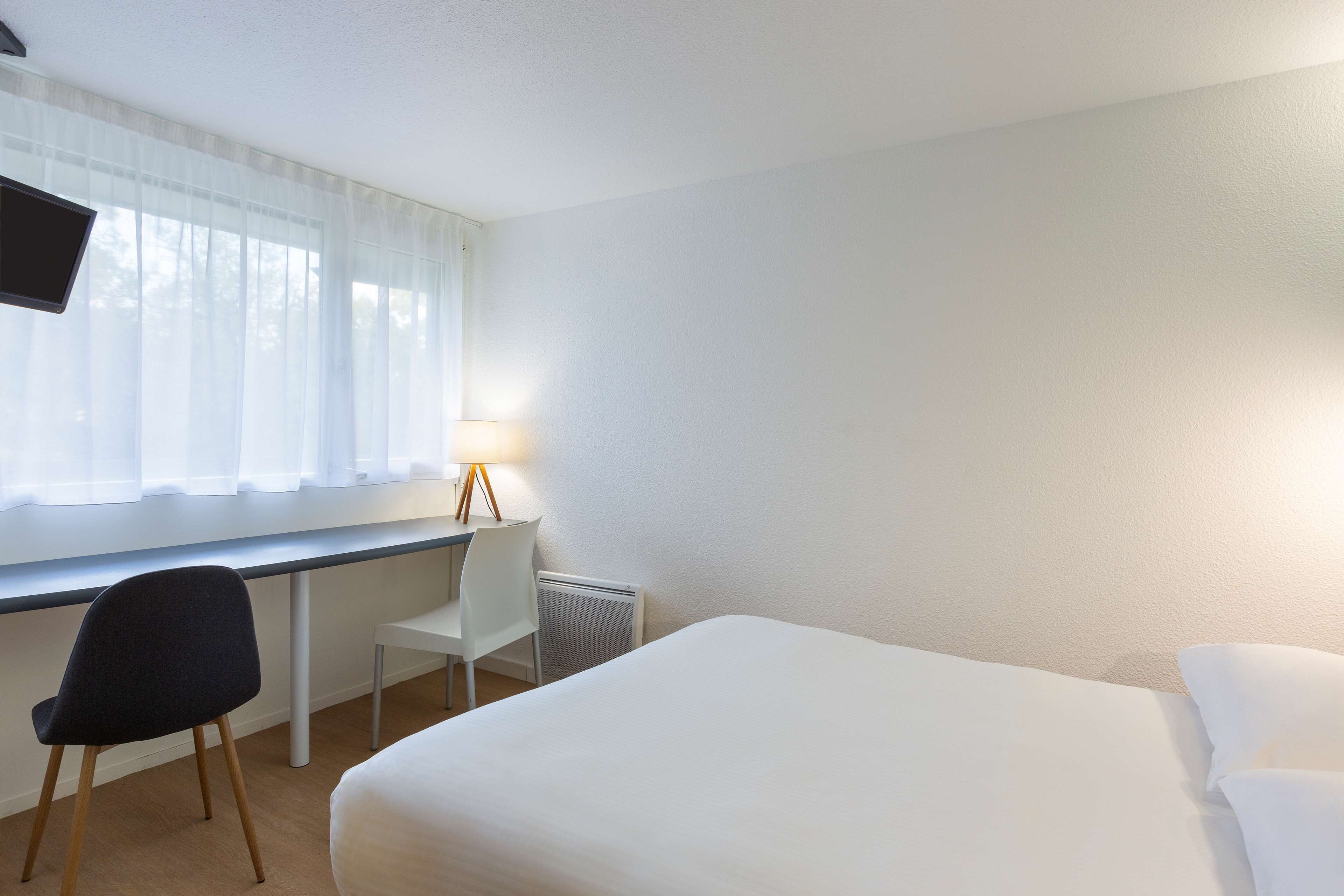 A hotel room with a bed, a desk, a chair, and a TV.