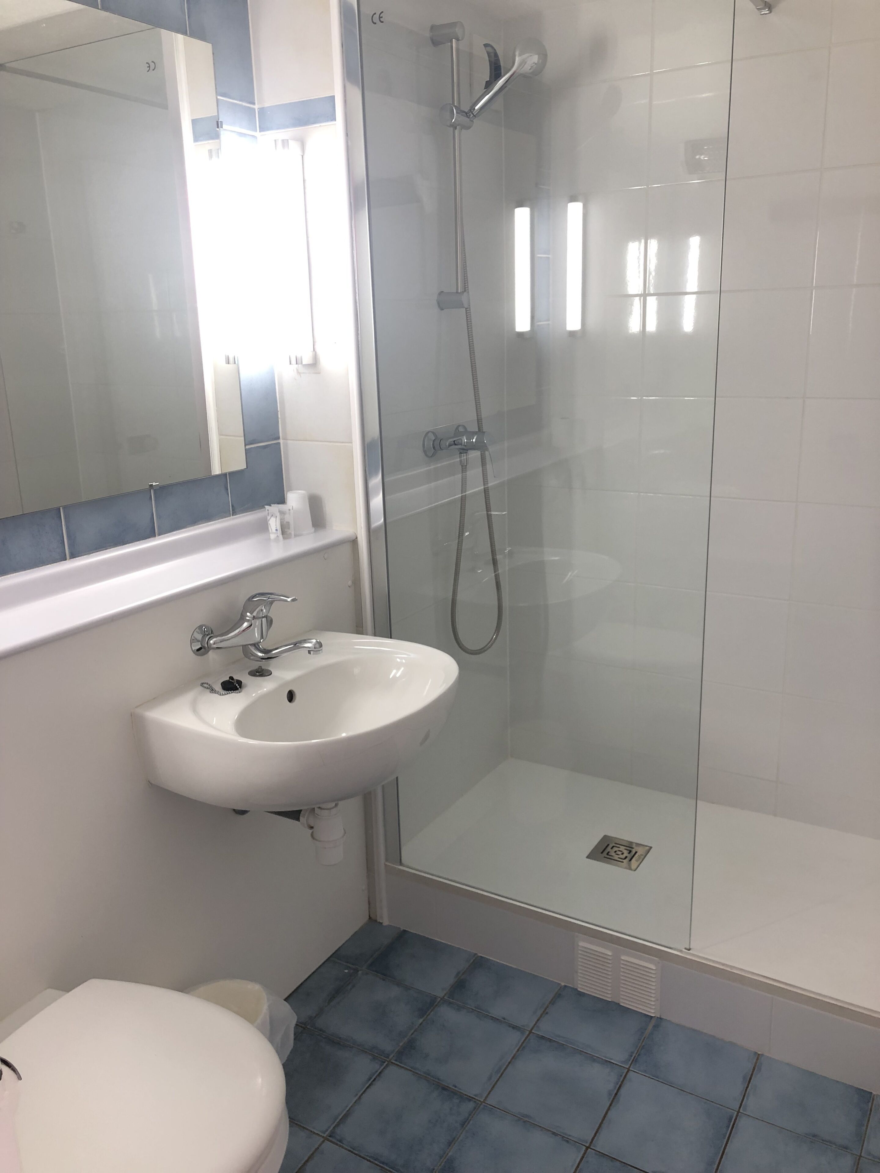 Une salle de bain avec un lavabo blanc, un miroir, une cabine de douche et des toilettes.