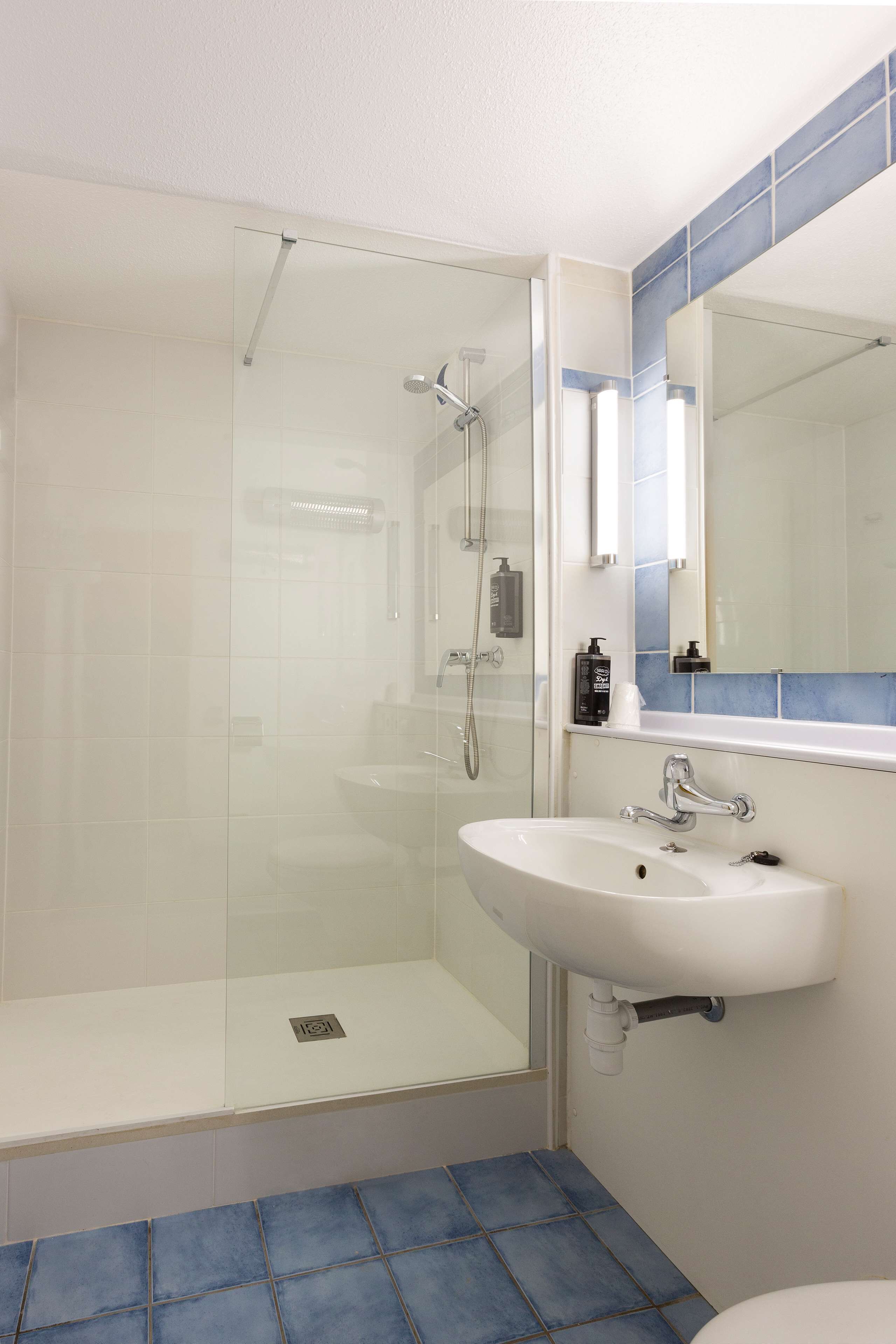 Un baño con ducha de vidrio, un lavamanos blanco y un espejo encima.