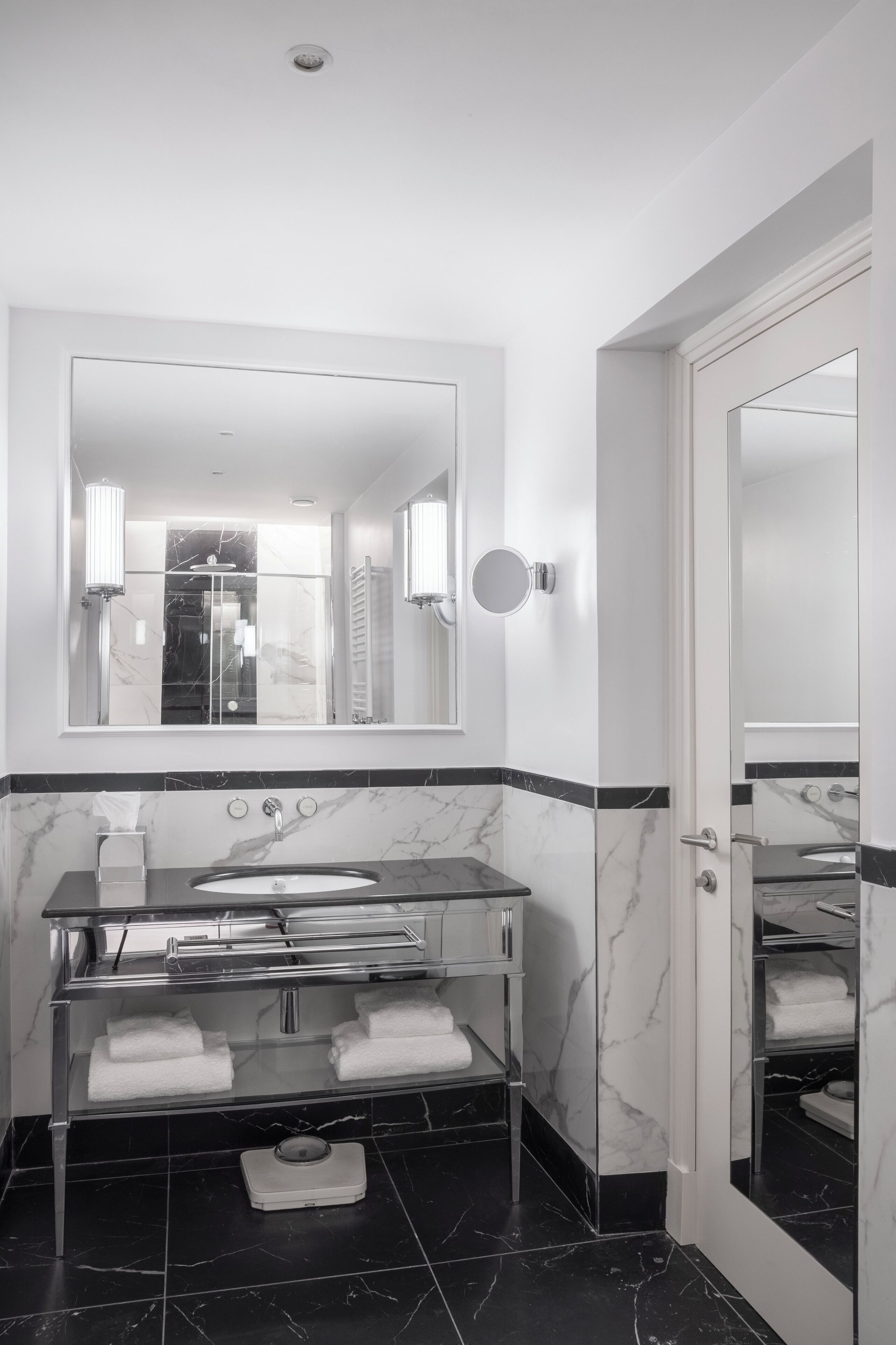 A modern bathroom with a large mirror, a marble-tiled floor, a built-in sink, and a towel rack.