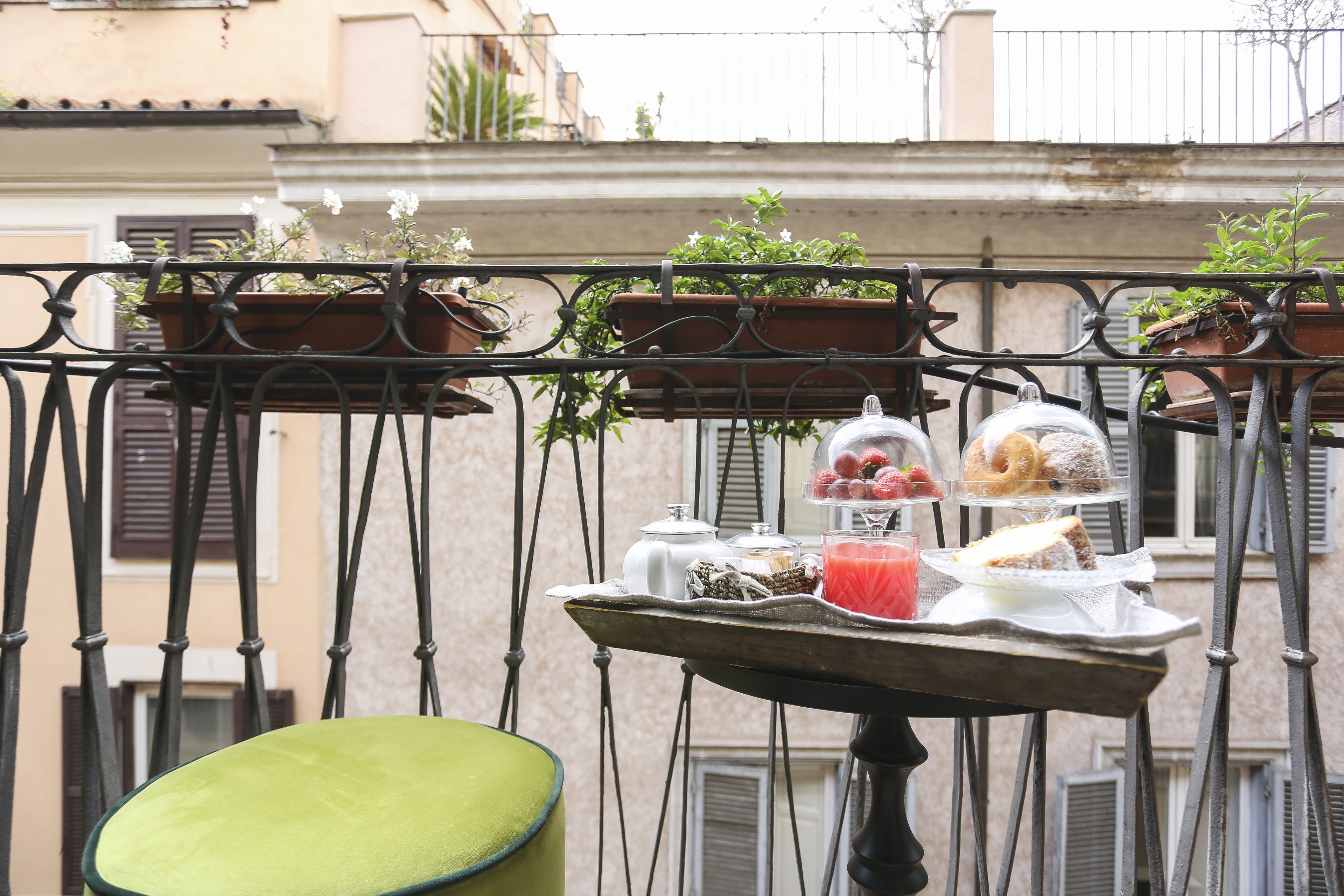 A balcony with a table set for breakfast, including pastries, fruits, and a drink.