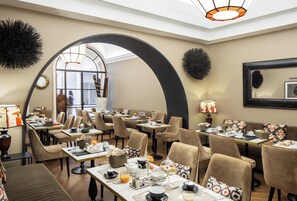 A dining area with multiple tables and chairs, a large arched doorway, and a view of the outside.