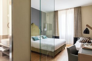 A hotel room with a bed, a desk, a chair, a lamp, and a window with curtains.