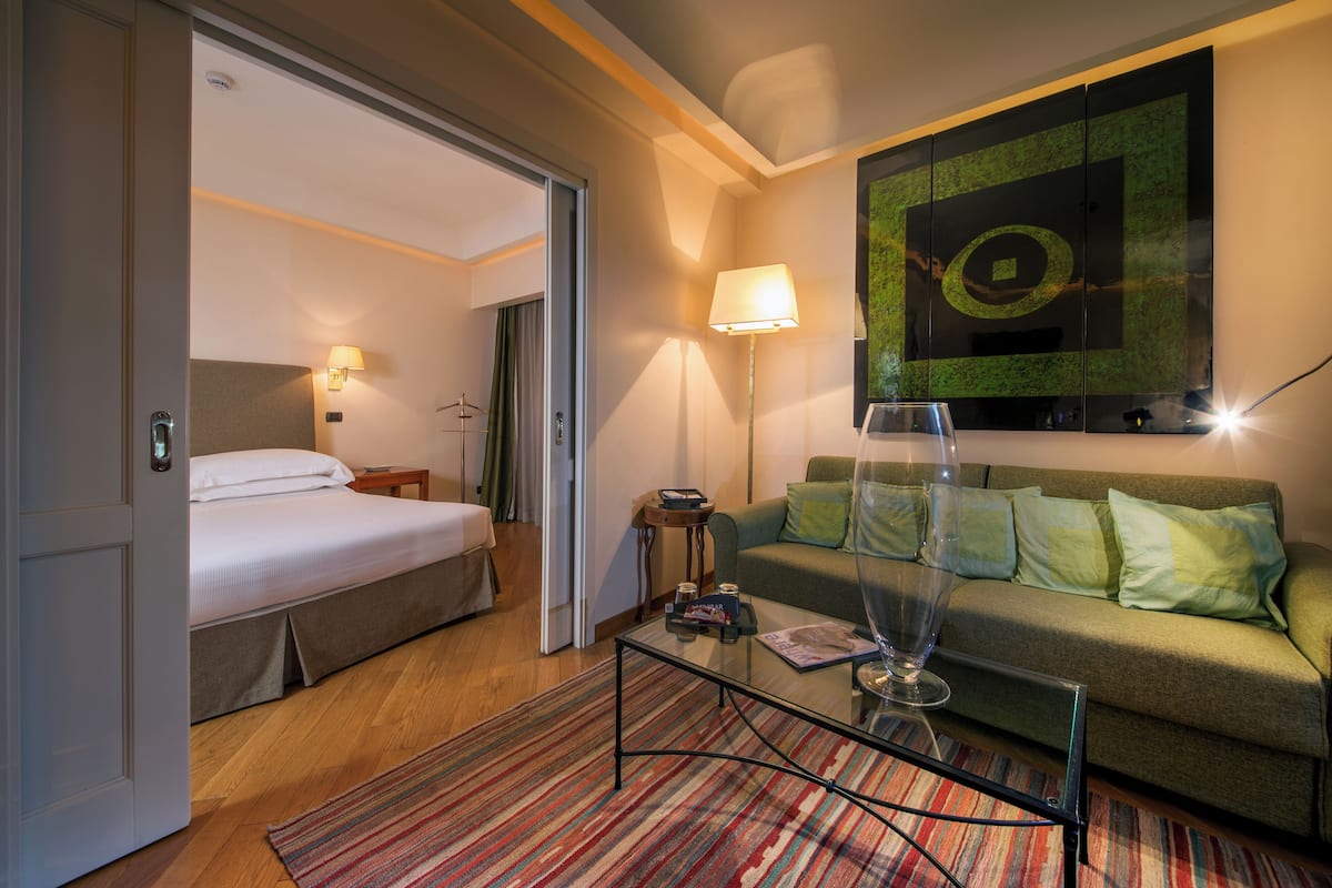 A hotel room with a bed, a sofa, a coffee table, and a painting on the wall.