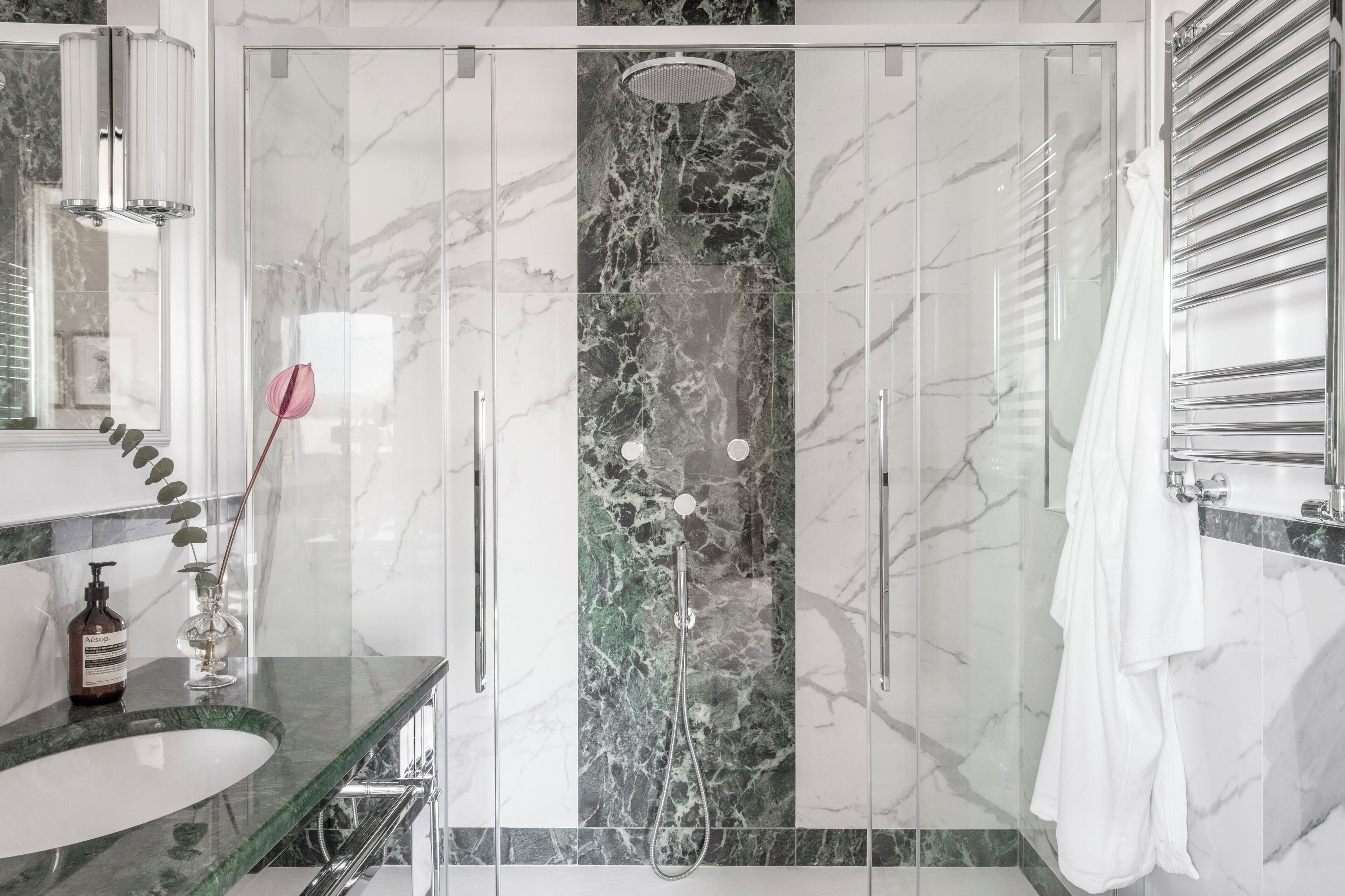 A modern bathroom with a glass-enclosed shower, marble walls, a sink with a green countertop, and a white towel hanging on the wall.