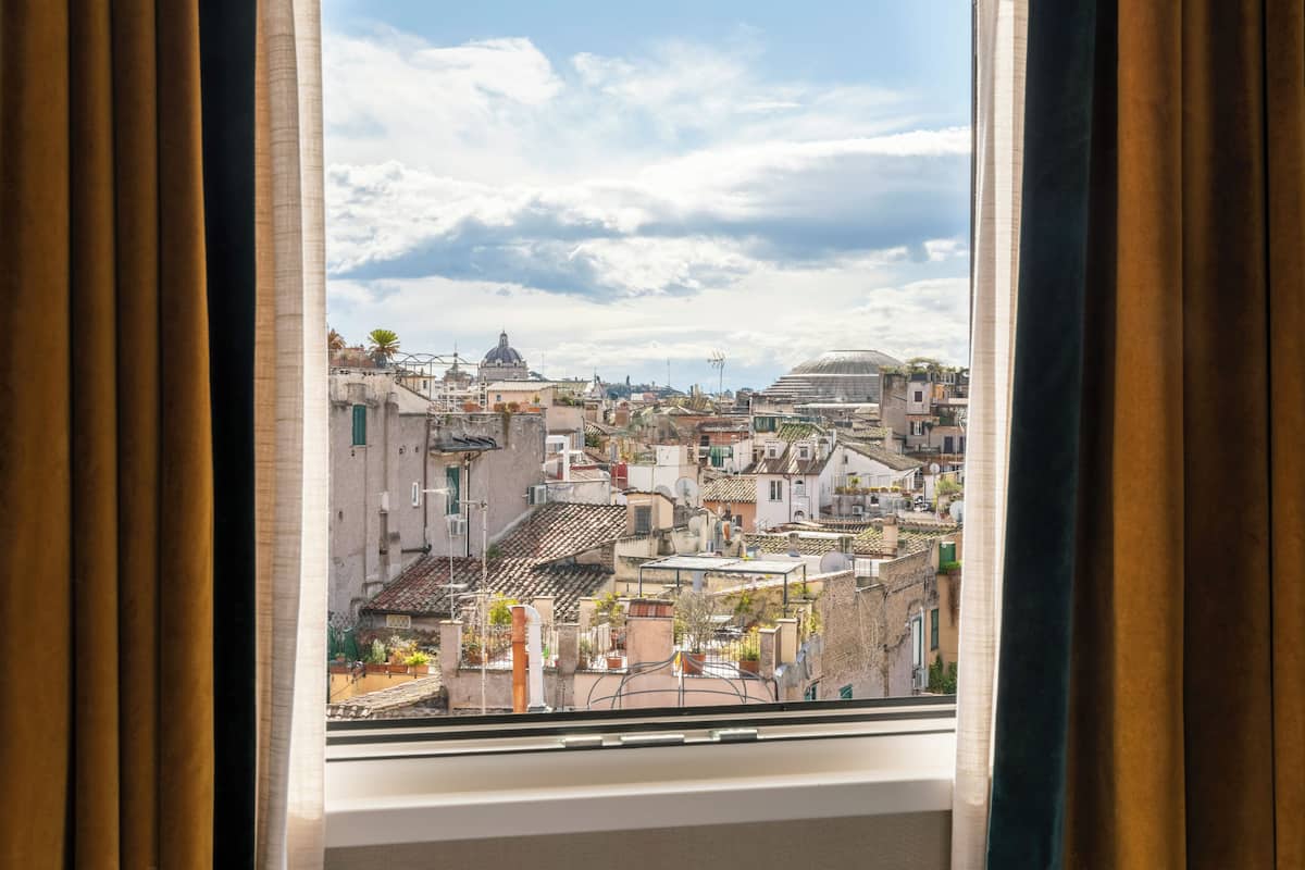 A view from a window with curtains, overlooking a densely packed urban area with various buildings and a clear sky.