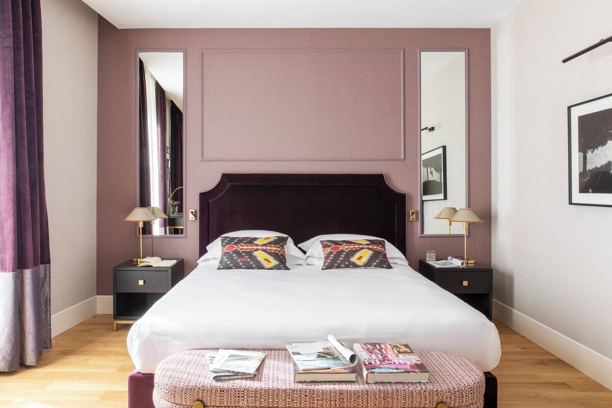 A neatly arranged bedroom with a large bed, two bedside tables, a mirror, and a small table with books and a phone.