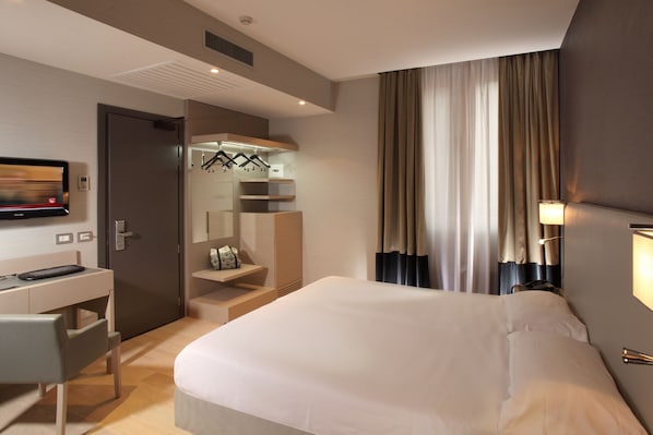 Habitació d'hotel moderna amb un llit gran, una taula de treball amb una cadira, un televisor i un armari.