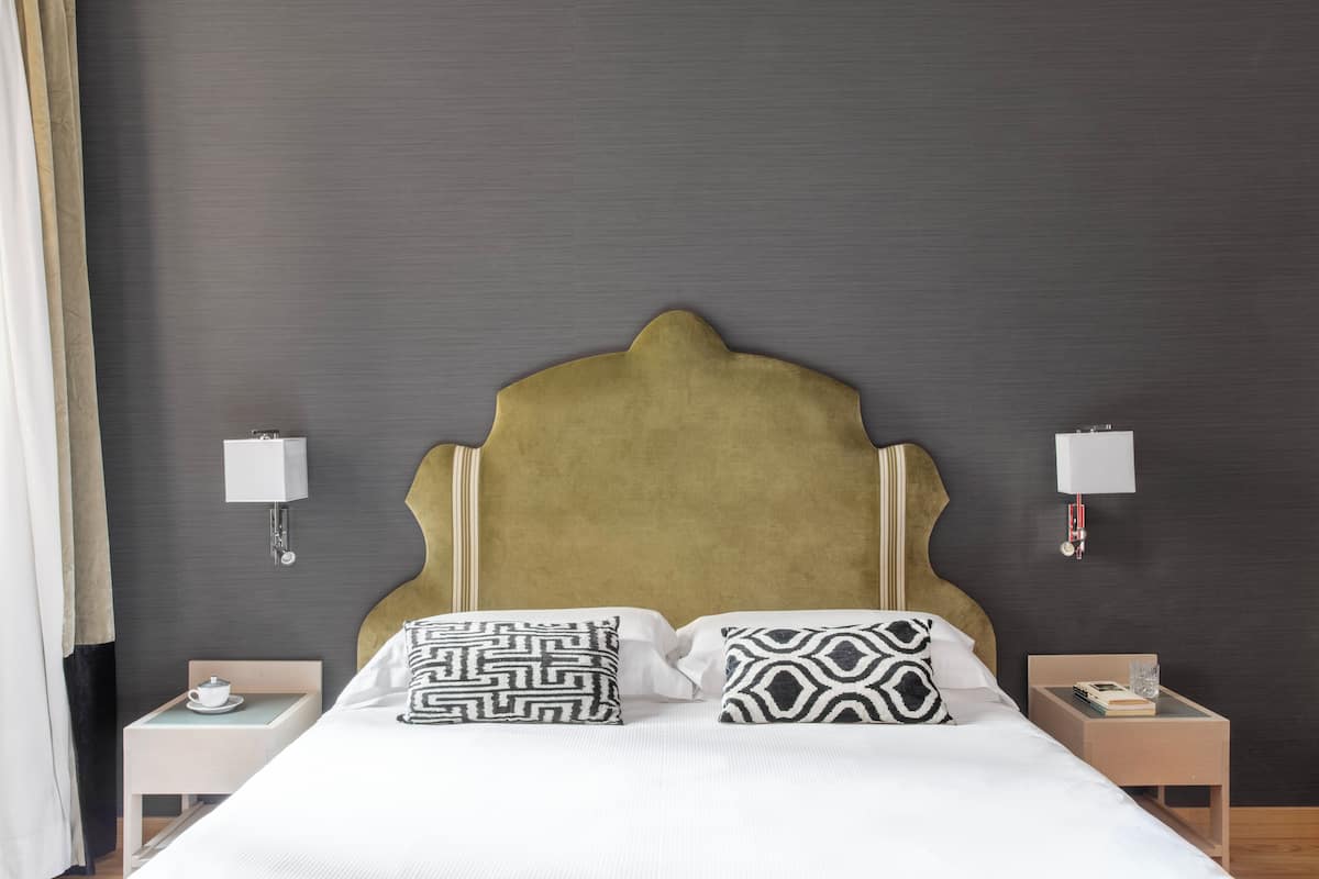 A neatly made bed with patterned pillows, a headboard, bedside tables with lamps, and a wall-mounted light fixture.
