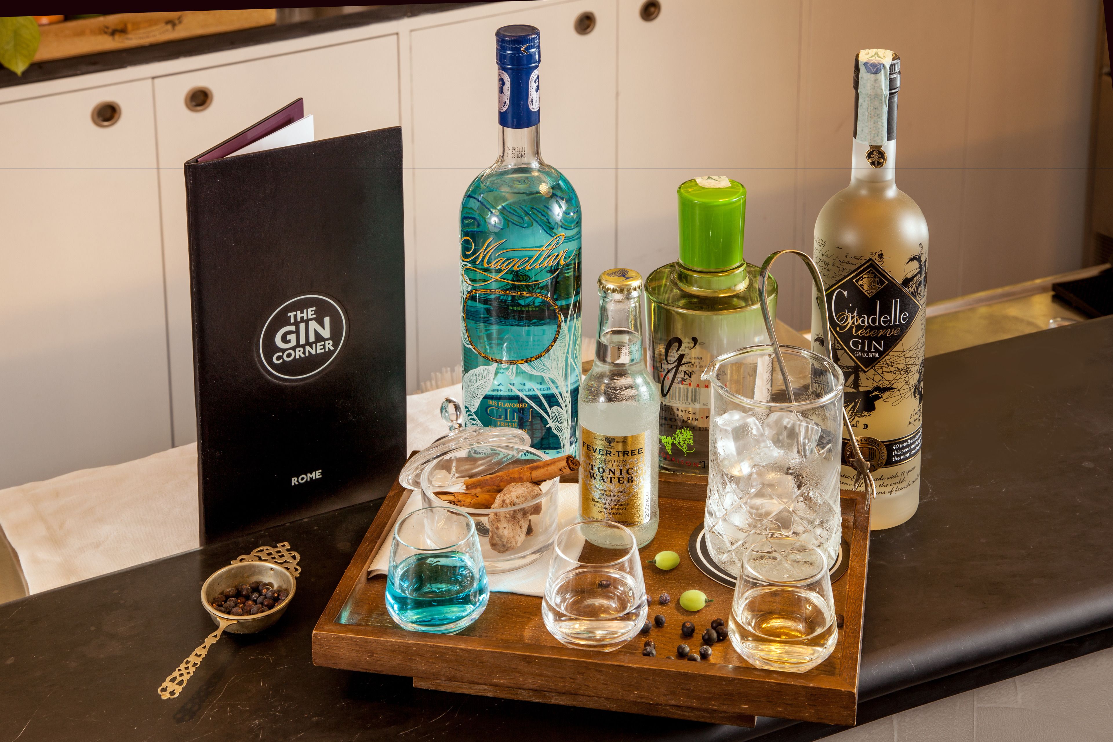 Una bandeja con diversas botellas y vasos de alcohol, incluyendo ginebra y agua tónica, sobre una mesa de madera.
