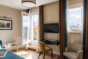 Camera d'albergo con una scrivania, una sedia, un letto, una televisione e una finestra con tende.