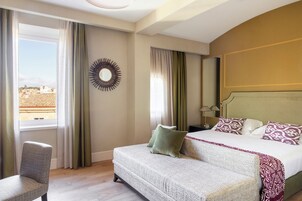 A hotel room with a bed, a sofa, a chair, a mirror, and a view of the city.