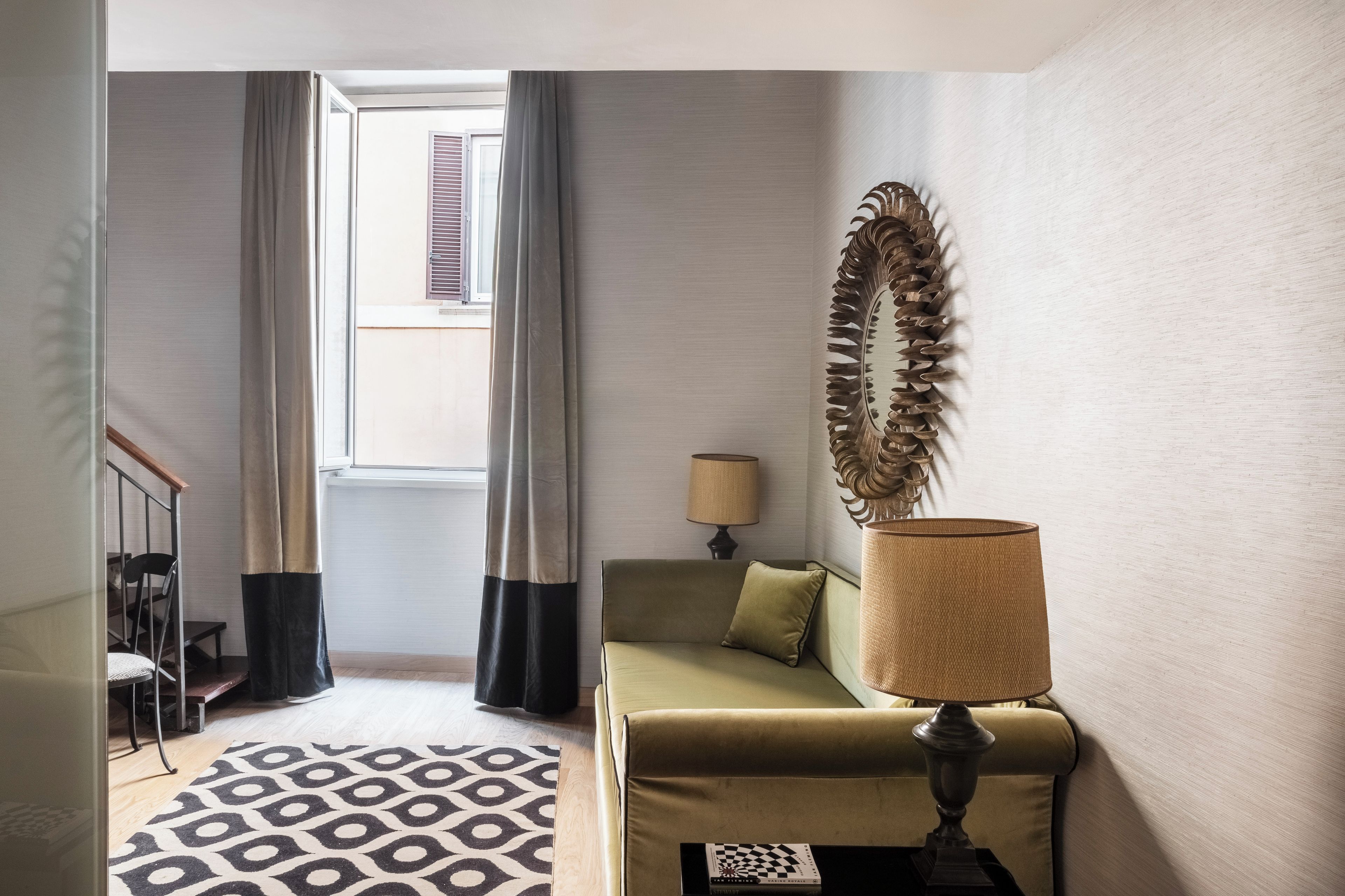 A room with a patterned rug, a sofa, a lamp, and a decorative mirror.