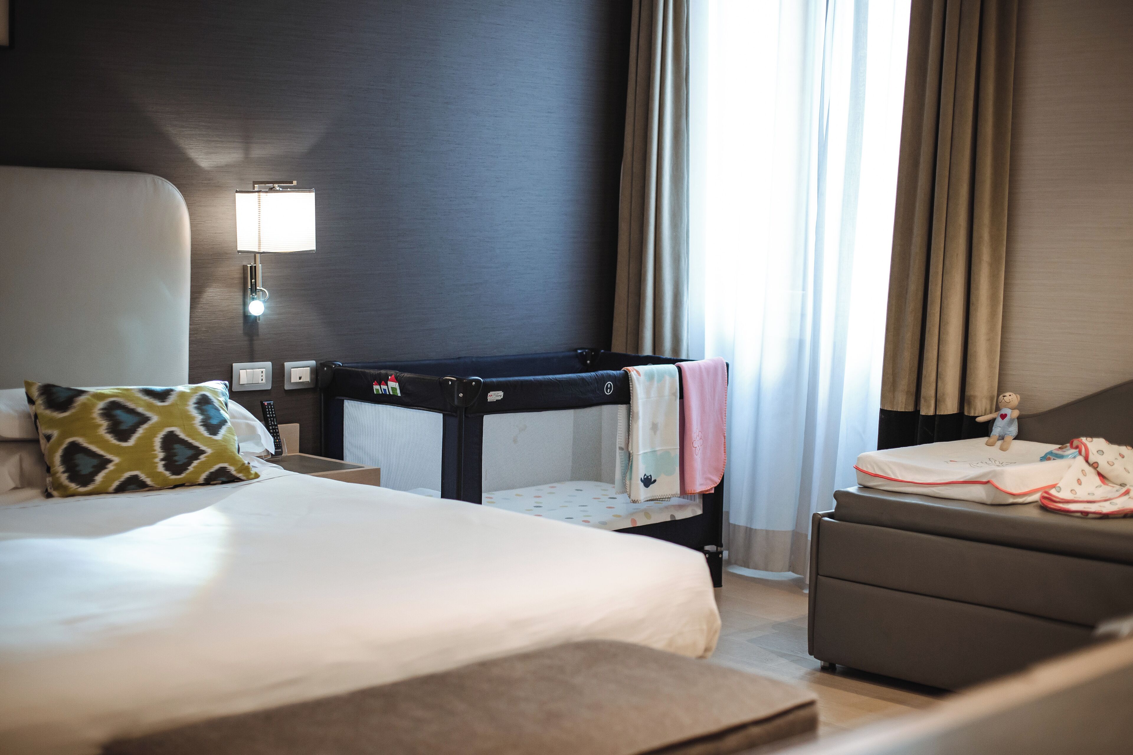 A hotel room with a large bed, a small desk, a crib, and a sofa.