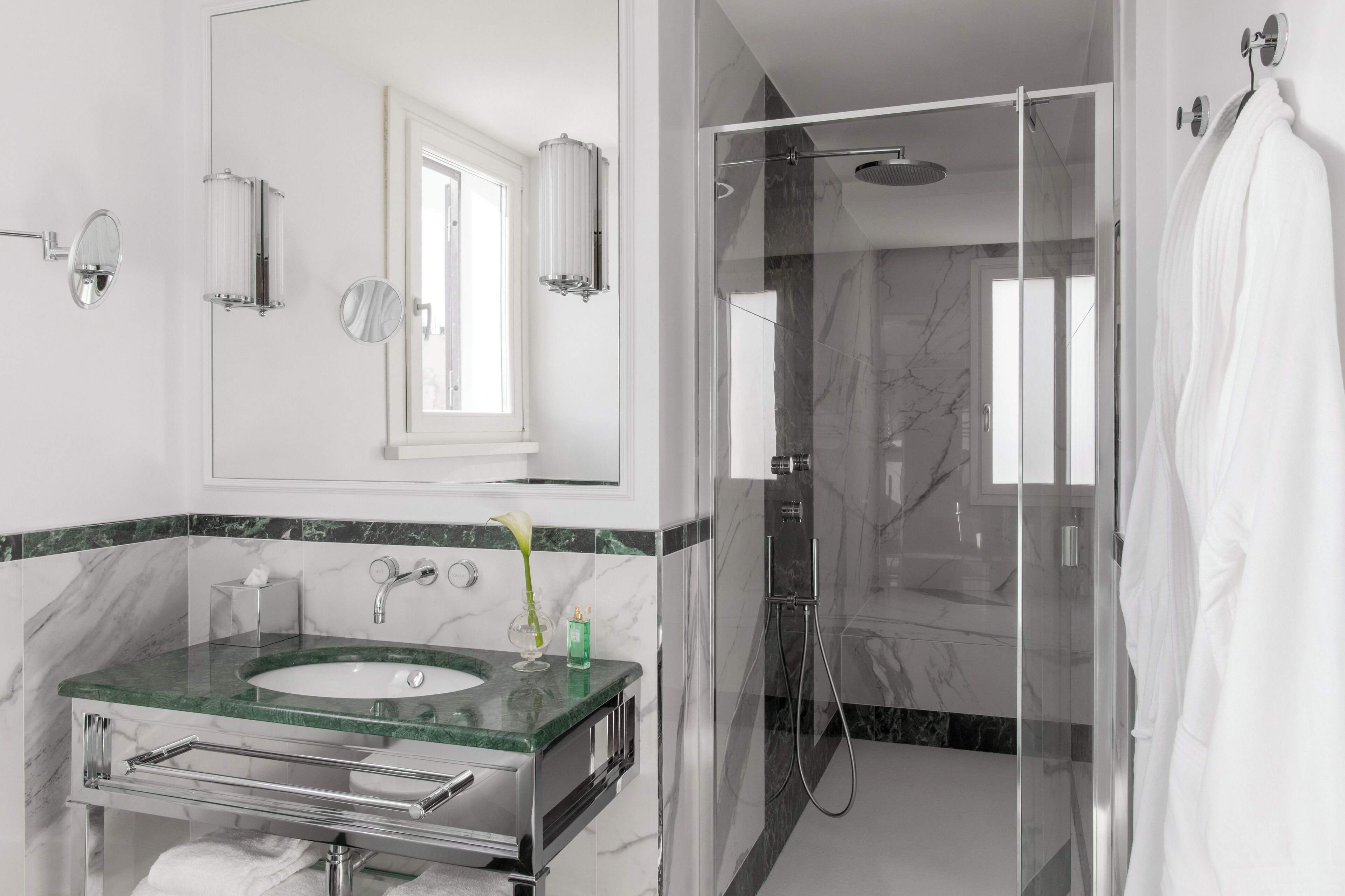 Un baño moderno con ducha de vidrio, lavamanos con azulejos de mármol y un espejo grande.