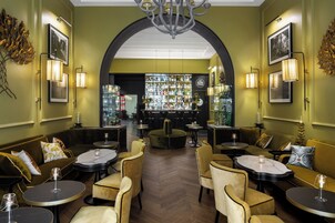 Zona de bar con diversas botellas de licores, un espacio de asiento con mesas y sillas redondas y un candelabro.