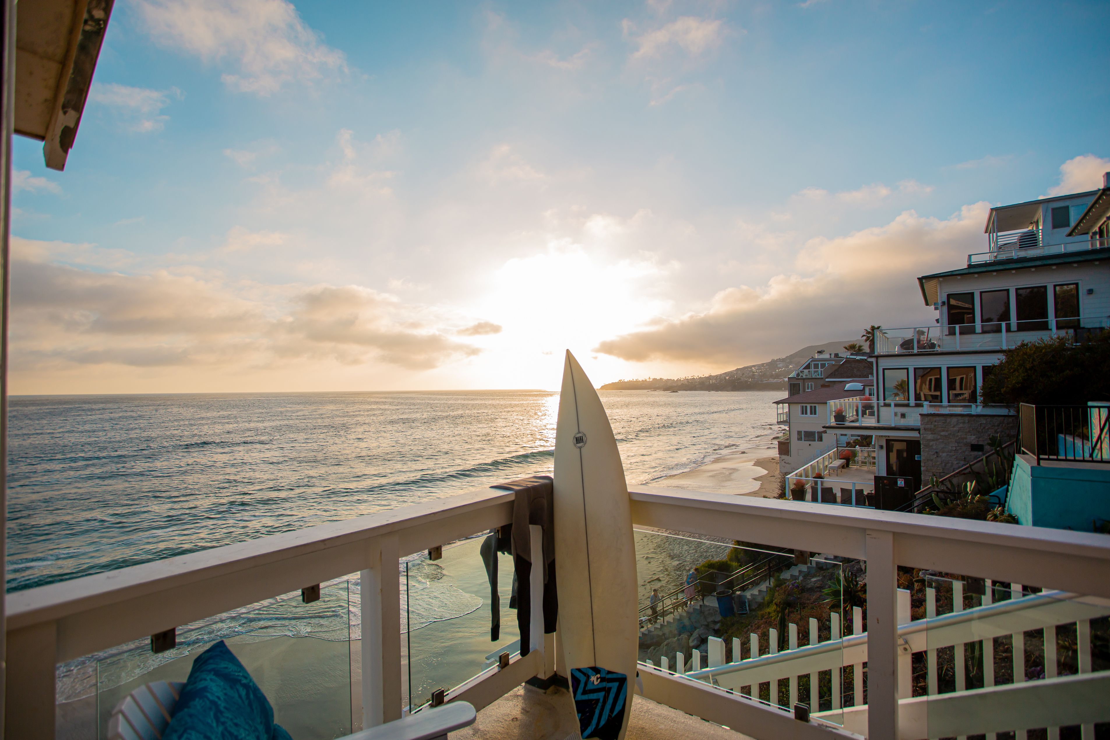A balcony with a view of the ocean and a surfboard leaning against the railing.
