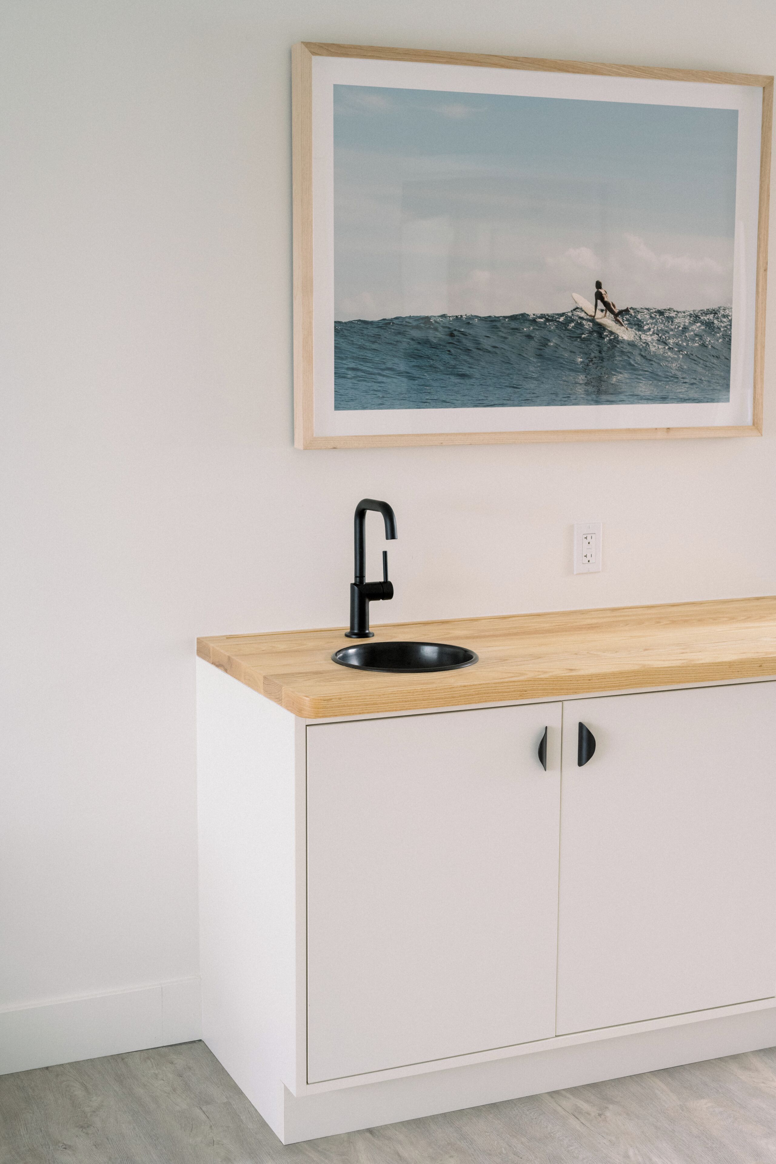 A kitchen with a wooden countertop, a black sink, and a framed picture of a surfer on the wall.