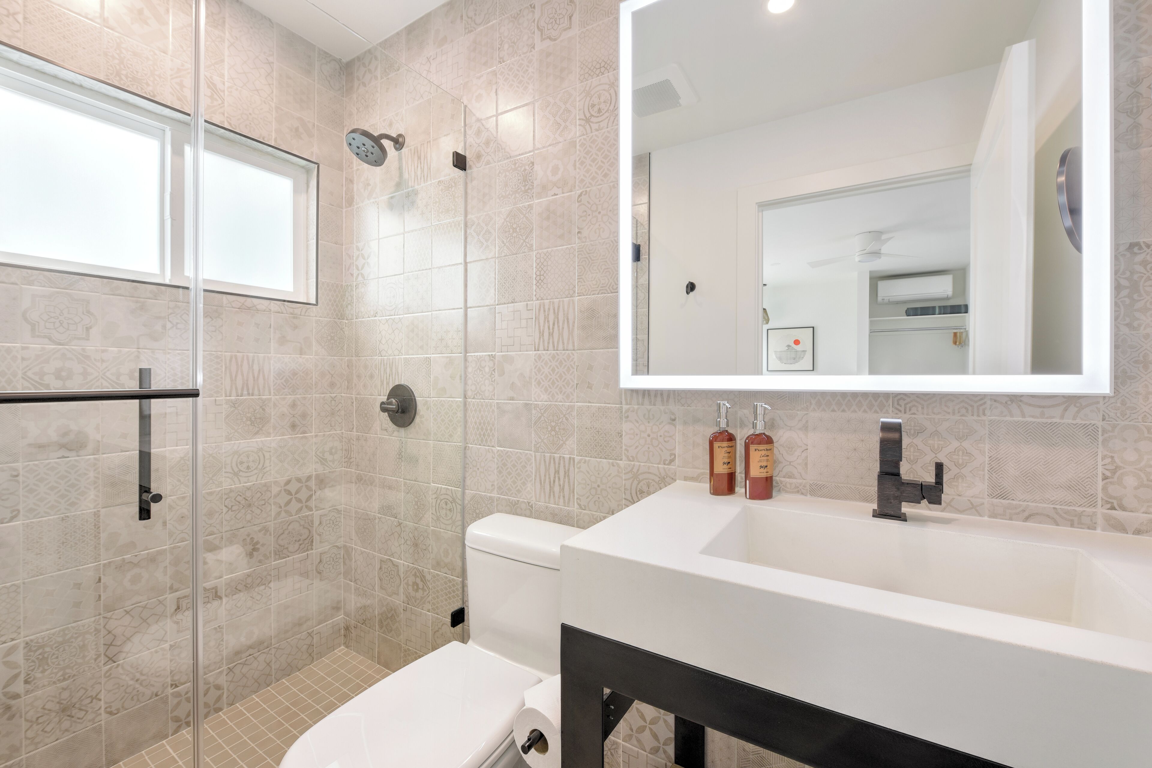 A modern bathroom with a glass-enclosed shower, a toilet, and a large sink with a mirror above it.