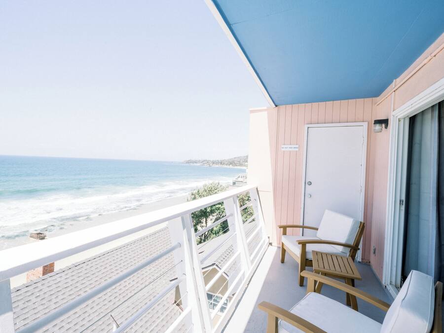 Un balcon donnant sur la plage, des chaises en bois et une porte.