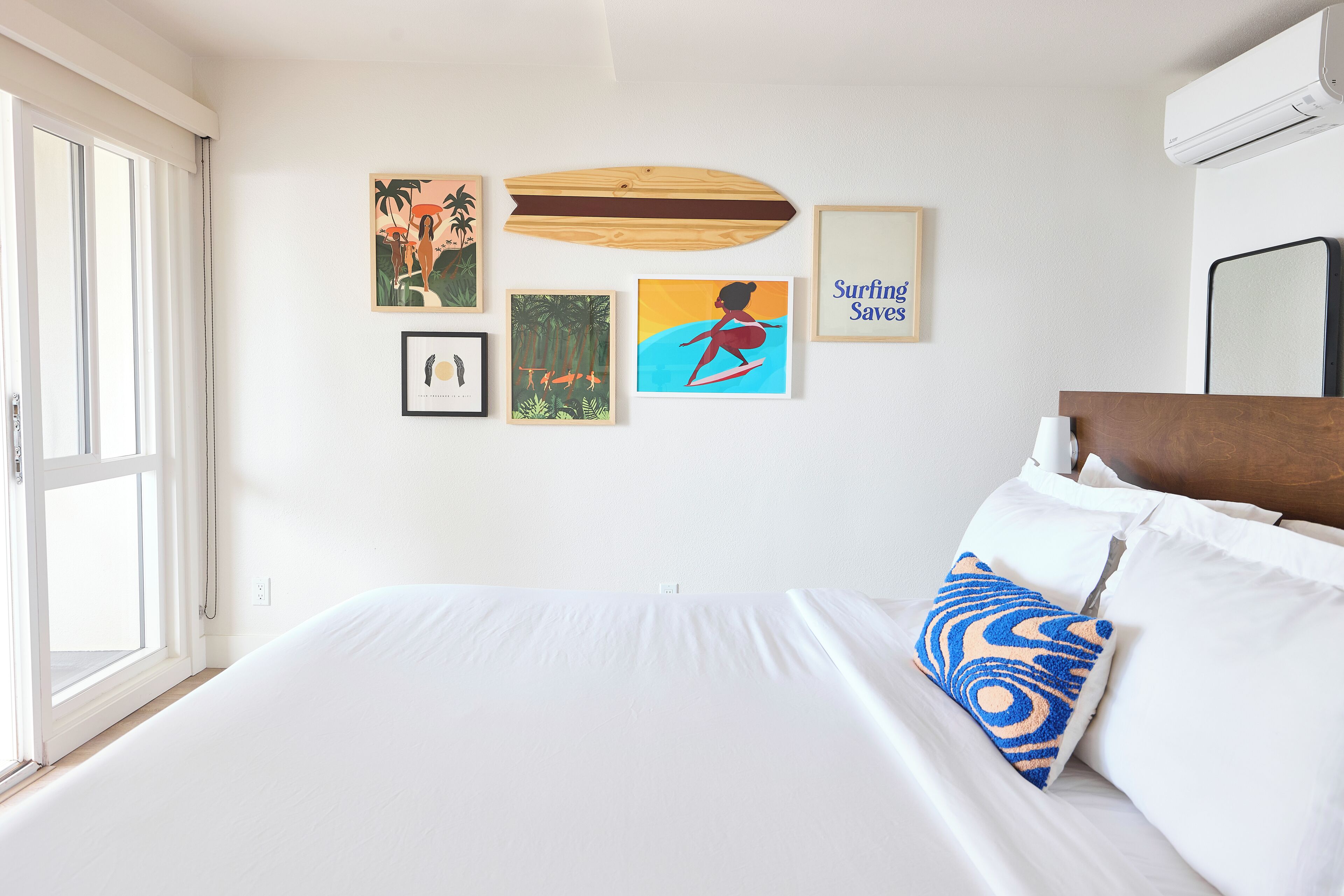 Une chambre avec un grand lit, du linge de lit blanc et une décoration murale représentant une planche de surf.