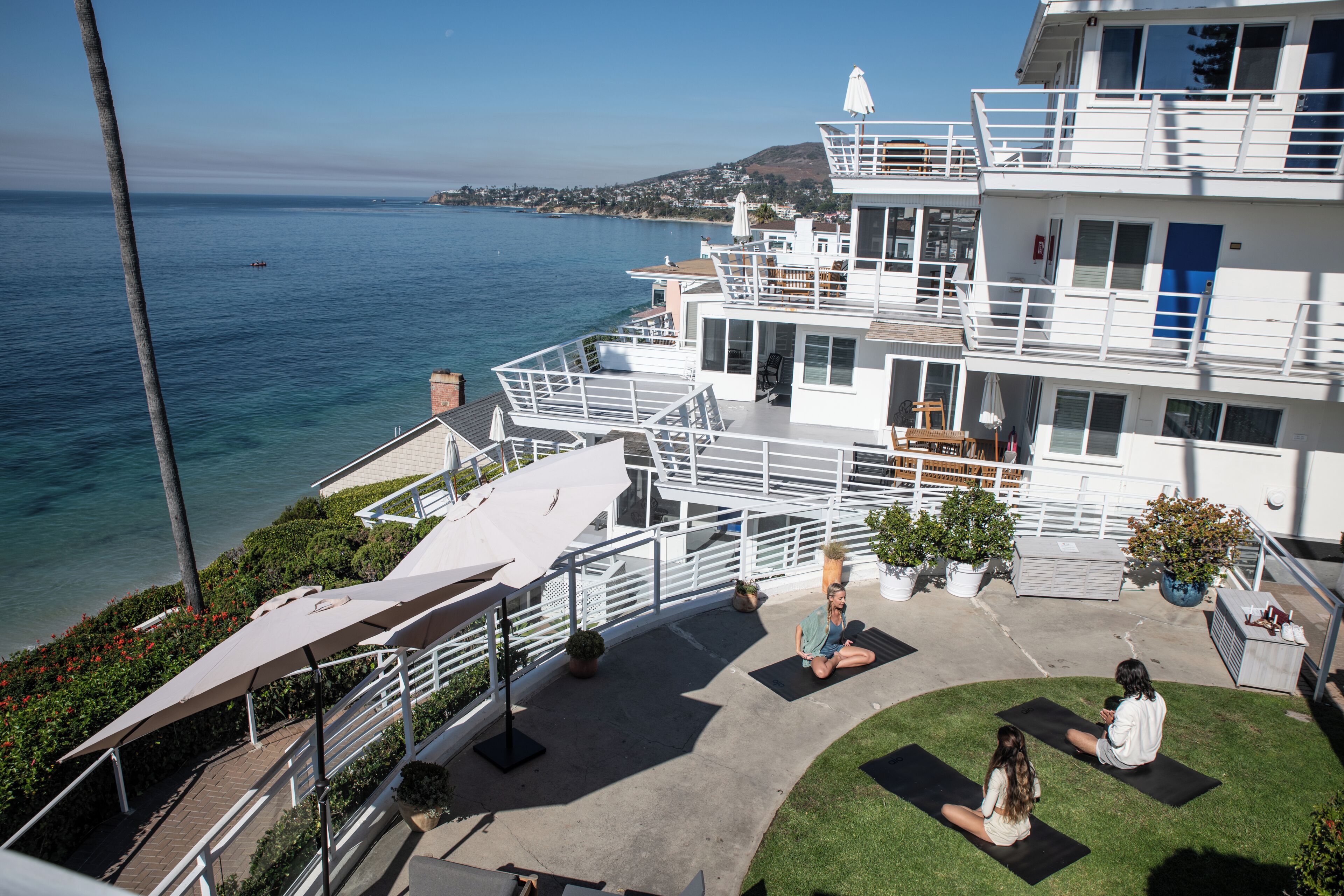 A multi-story building with balconies overlooking a body of water, a rooftop area with seating, and a grassy courtyard.