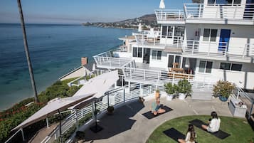 A multi-story building with balconies overlooking a body of water, a rooftop area with seating, and a grassy courtyard.
