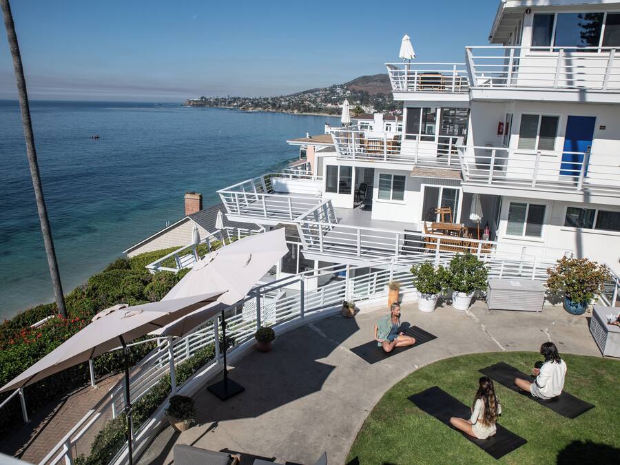 A multi-story building with balconies overlooking a body of water, a rooftop area with seating, and a grassy courtyard.