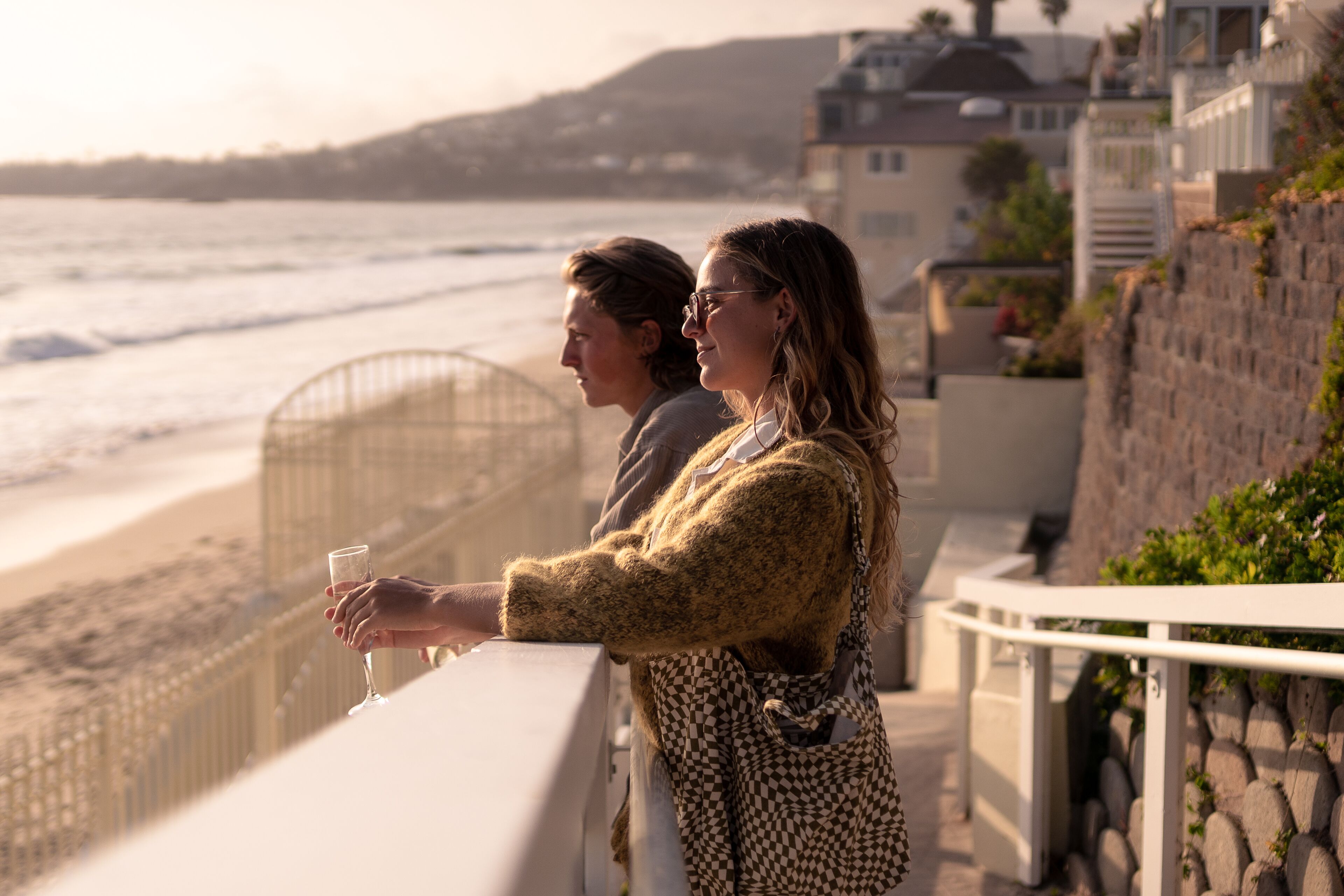 A balcony overlooking a beach with a railing and a glass of wine.