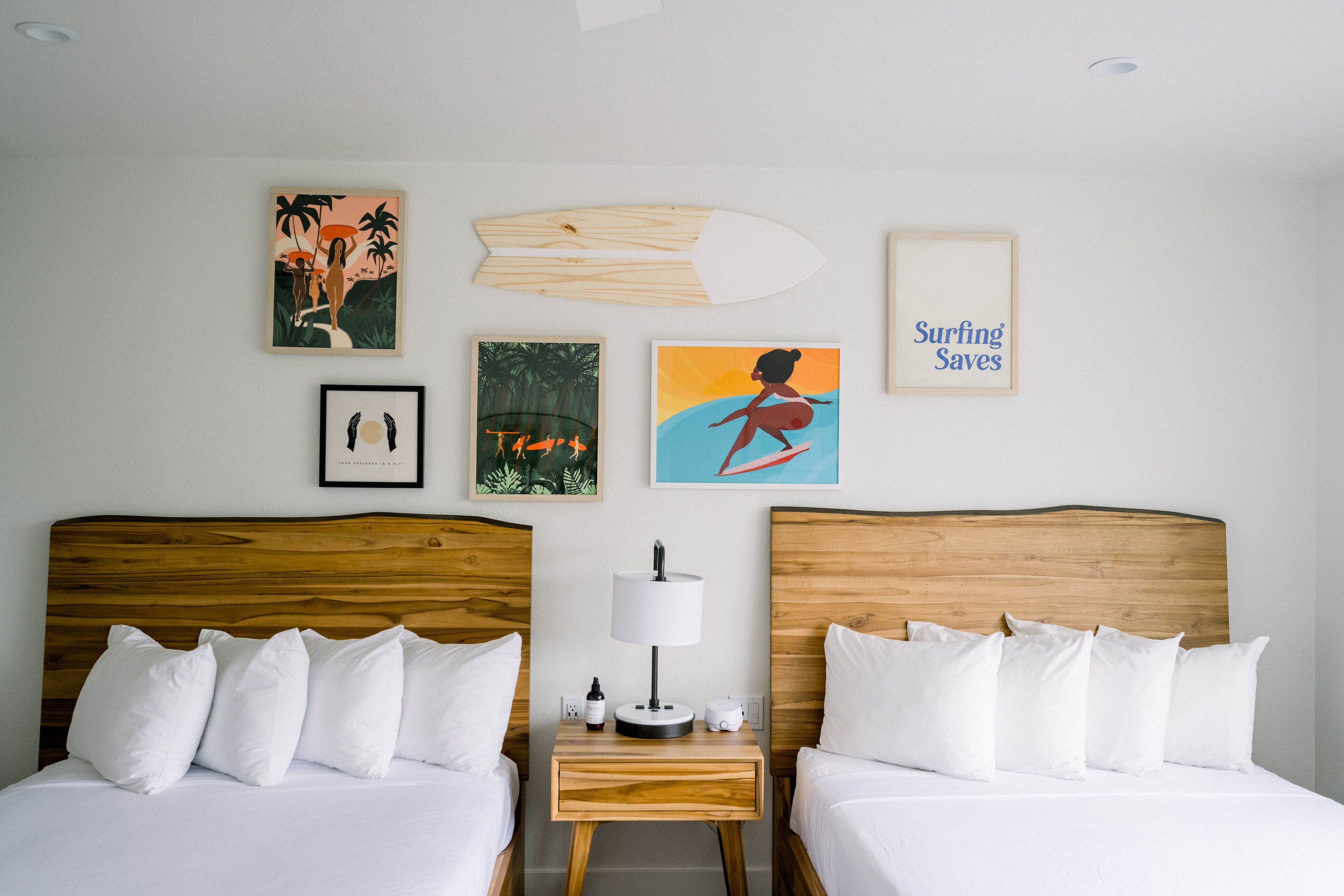 Une chambre d’hôtel avec deux lits, une table de chevet avec une lampe et des œuvres d’art accrochées aux murs.