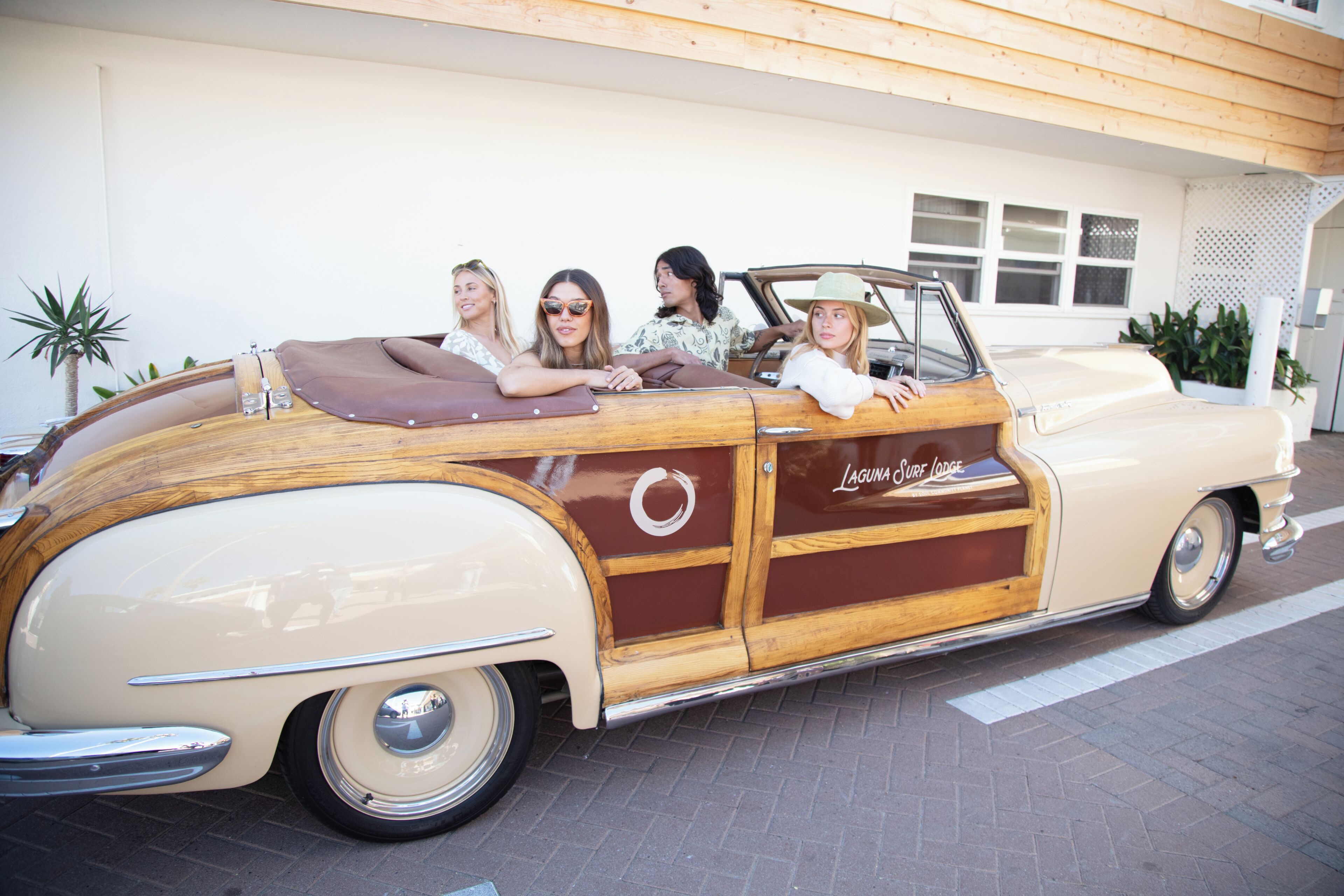Un coche descapotable antiguo con pasajeros estacionado frente a un edificio con fachada de madera y un letrero que dice 'Laguna Surf Lodge'.