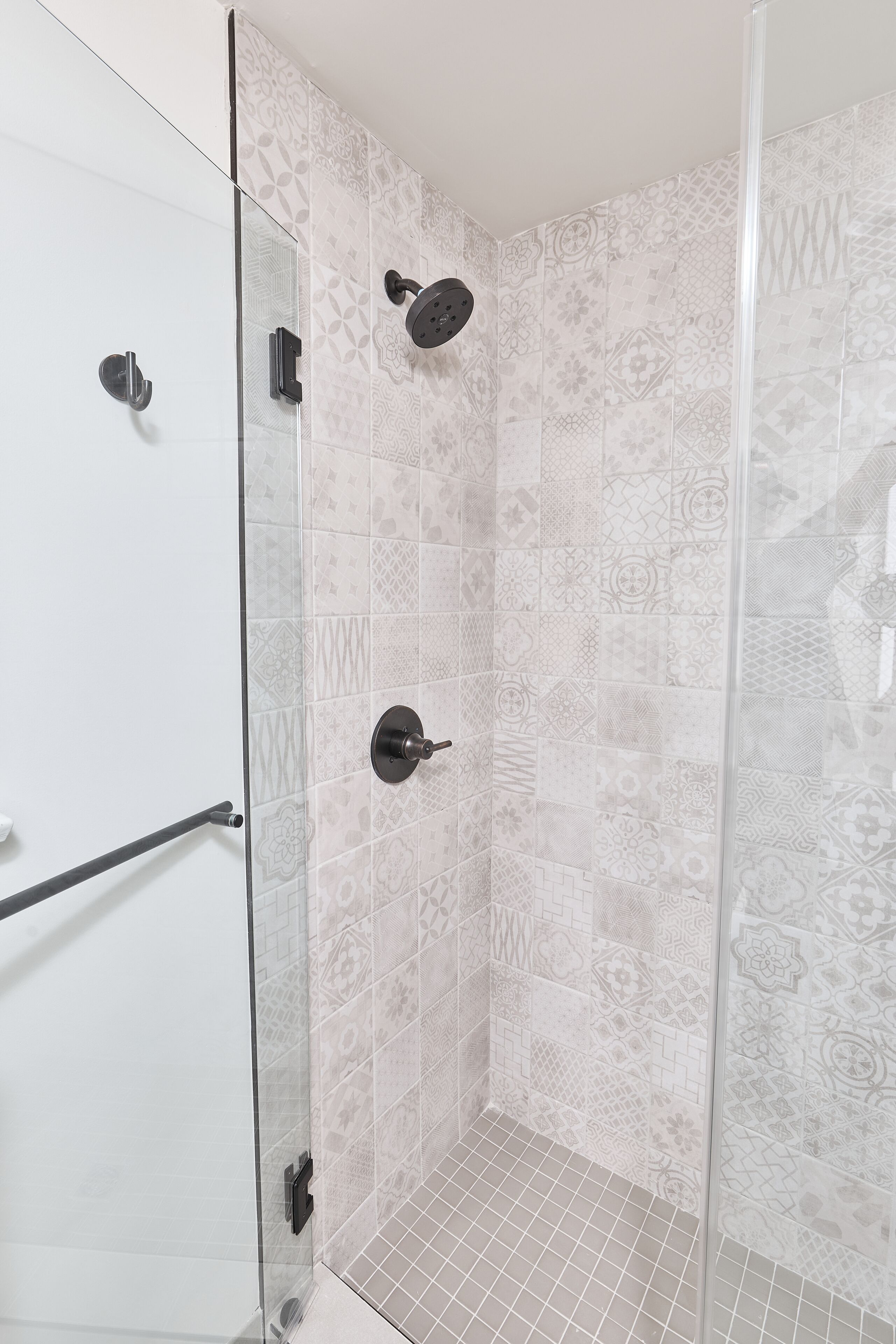 Ducha con puerta de cristal, azulejos estampados y barandilla.