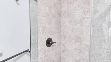 Ducha con puerta de cristal, azulejos estampados y barandilla.