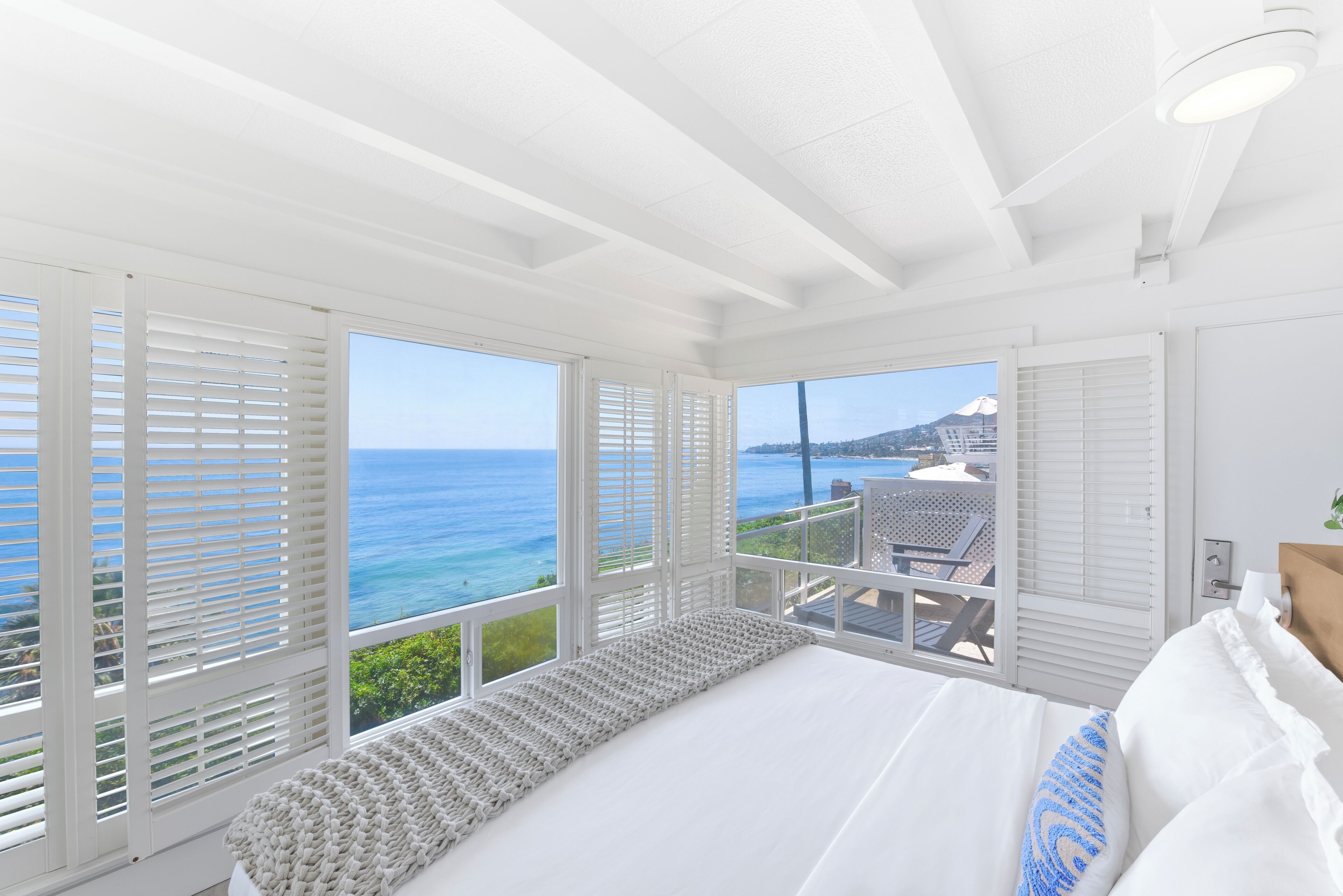 Ein Schlafzimmer mit einem großen Bett, weißen Wänden und Meerblick durch große Fenster.