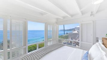Ein Schlafzimmer mit einem großen Bett, weißen Wänden und Meerblick durch große Fenster.