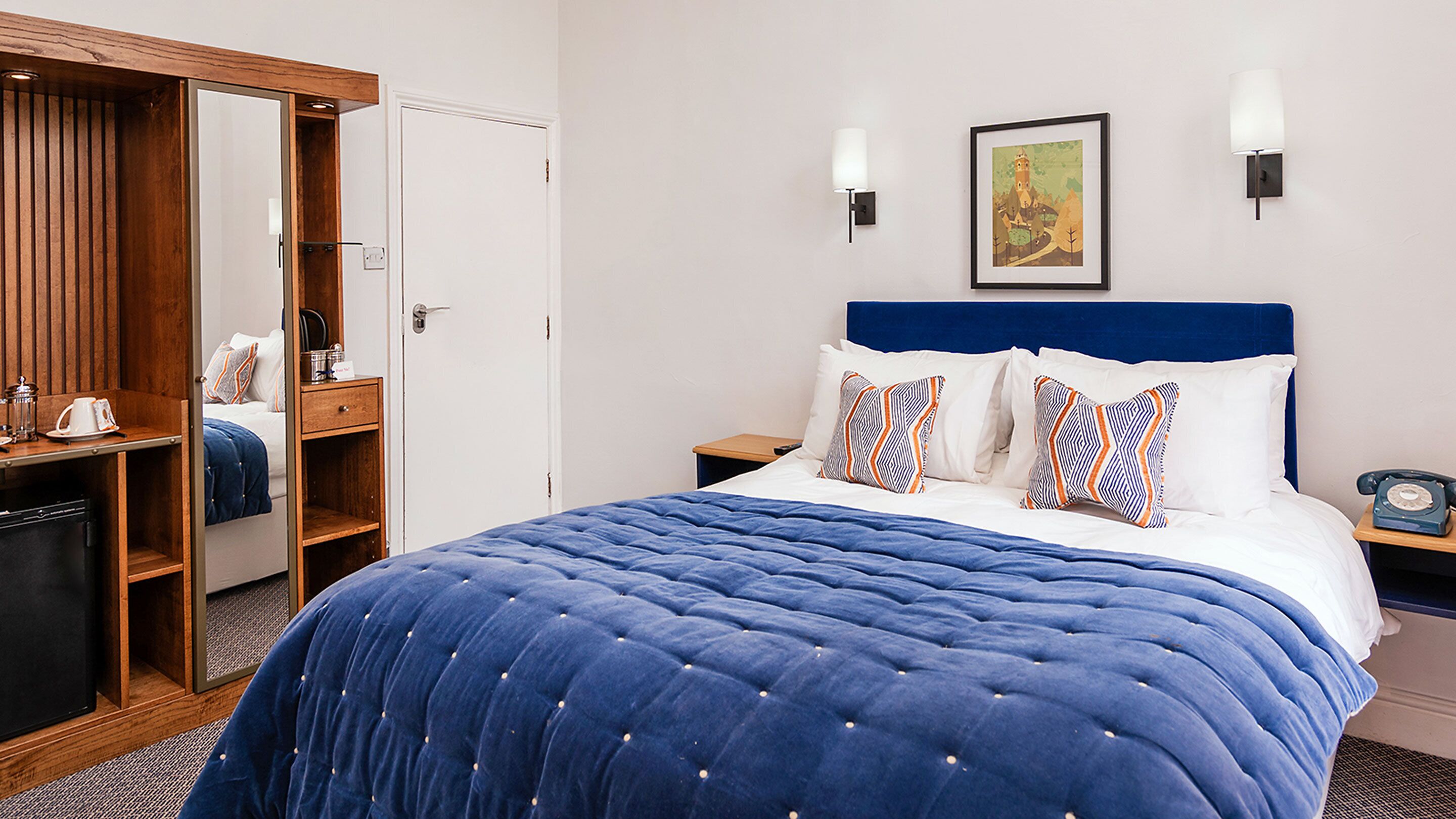 Ein Hotelzimmer mit einem großen Bett, einem Kleiderschrank, einem Nachttisch mit Lampe und einem Bild an der Wand.