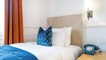 A hotel room with a bed, a blue patterned pillow, white pillows, a blue telephone, and a lamp on the nightstand.