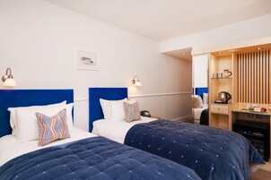 A hotel room with two beds, a desk, a mirror, and a minibar.