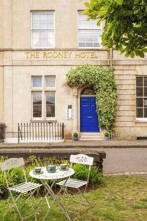 A building labeled 'The Rodney Hotel' with a blue door, a black iron fence, and a small table with chairs outside. - Rodney Hotel (Bristol)