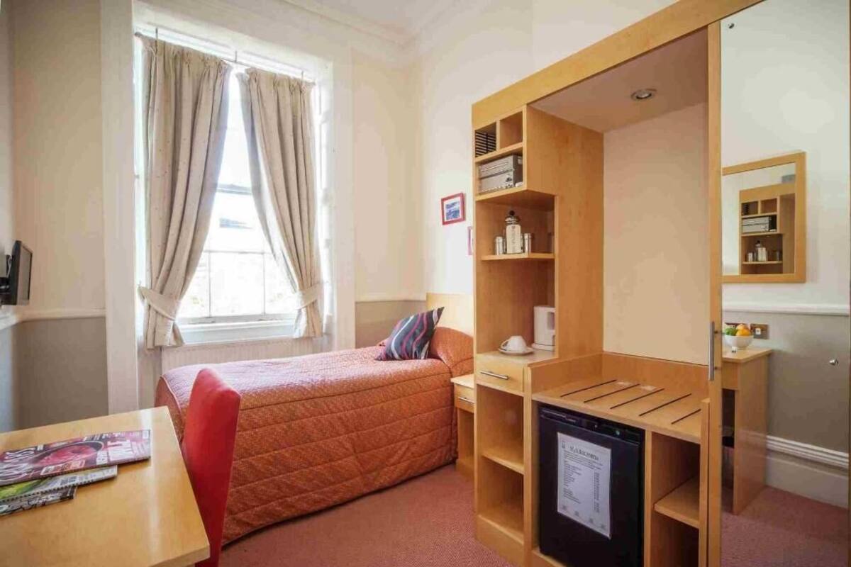 A compact hotel room with a bed, a desk, a built-in wardrobe, and a small kitchenette.