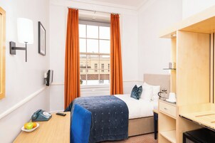 Ein Hotelzimmer mit einem Bett, einem Schreibtisch mit Lampe, einem Telefon und einer Obstschale.